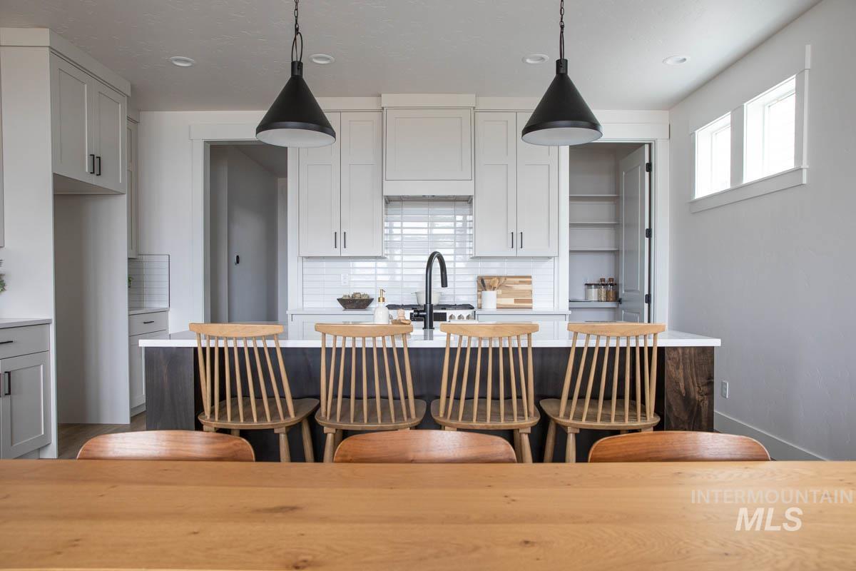 Kitchen featuring decorative light fixtures, a kitchen island with sink, backsplash, light stone countertops, and recessed lighting