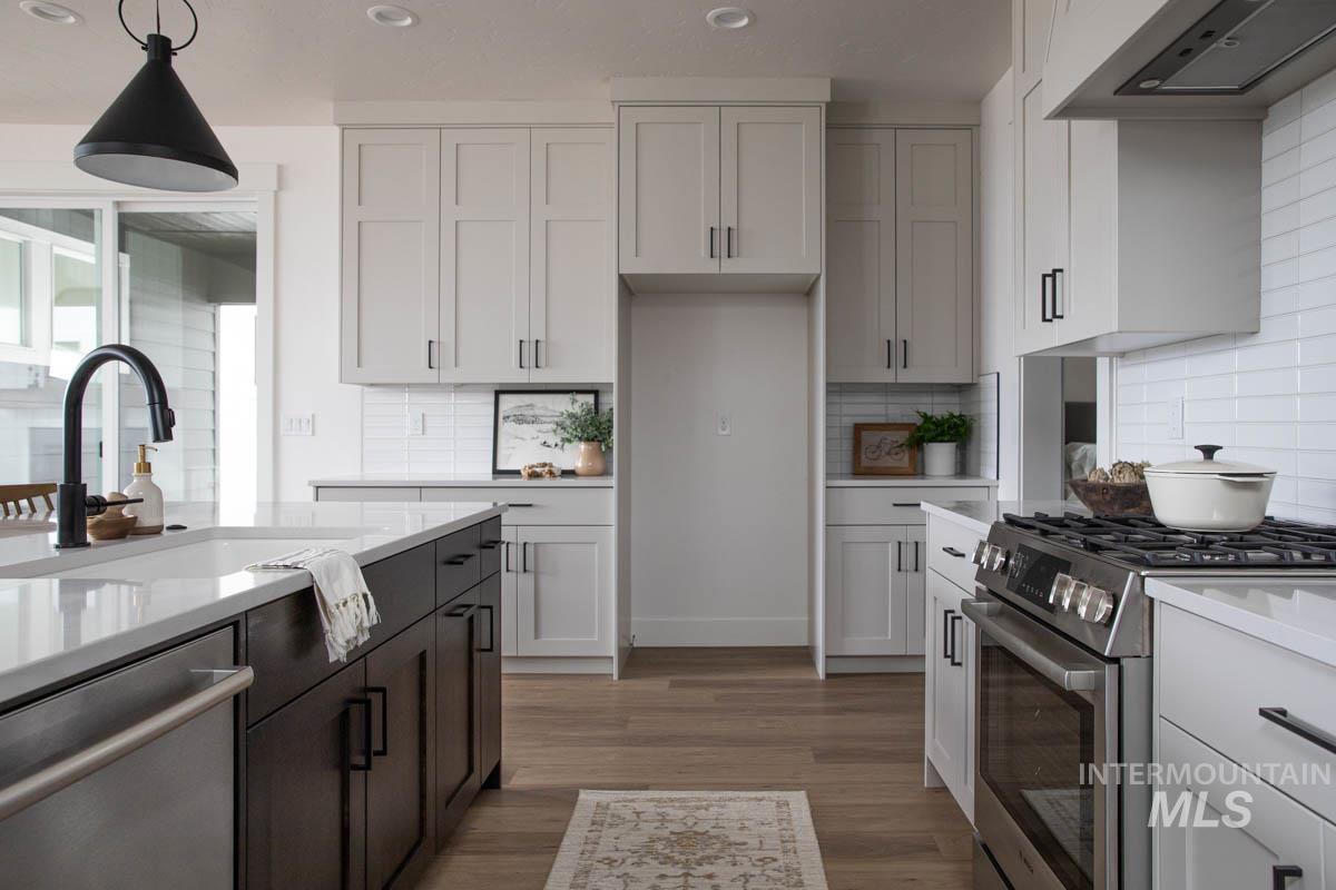 Kitchen with stainless steel appliances, white cabinetry, exhaust hood, hanging light fixtures, and light wood-style flooring
