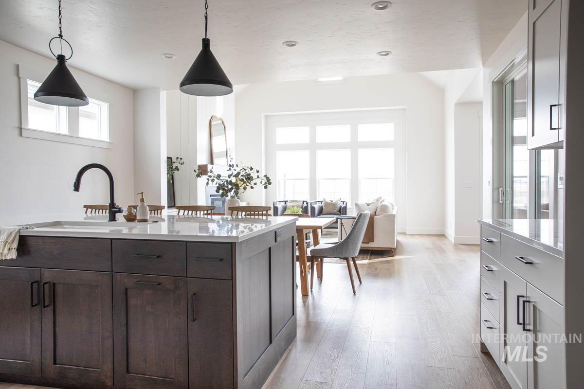 Kitchen featuring pendant lighting, light wood-type flooring, dark brown cabinetry, light stone countertops, and open floor plan