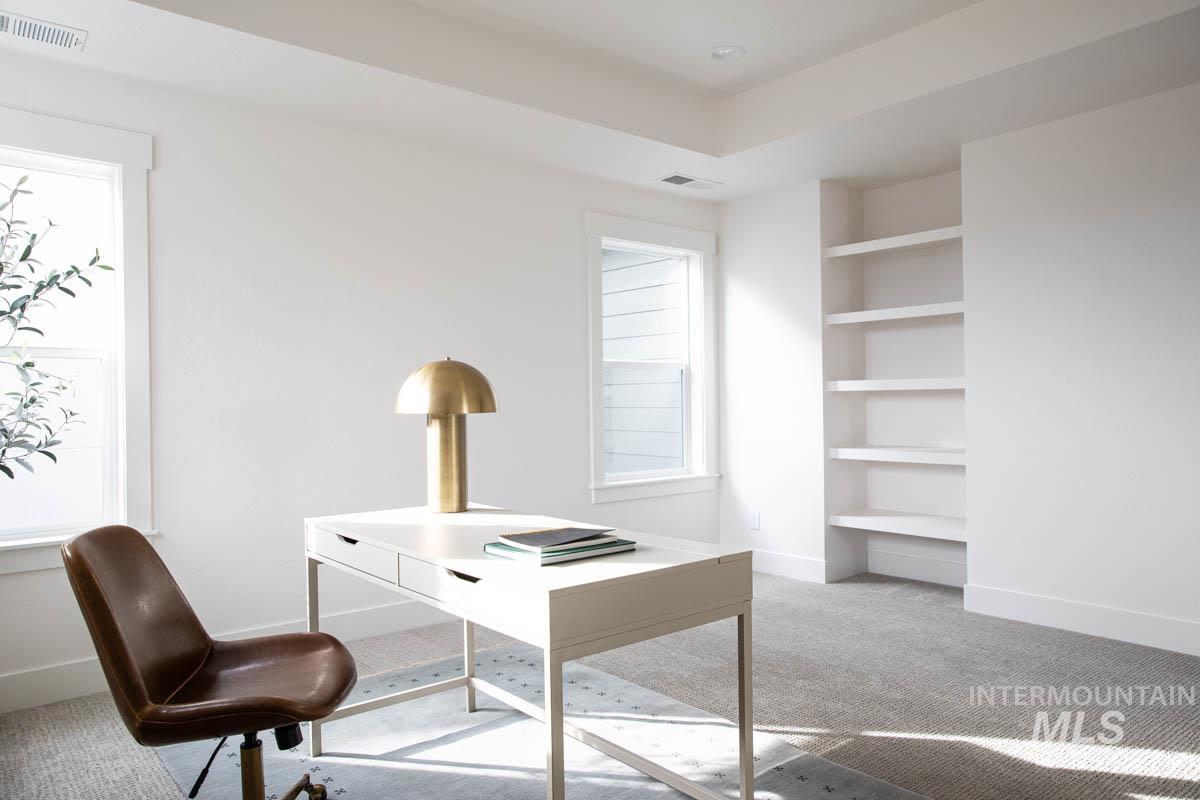 Office space featuring light colored carpet, built in shelves, and a tray ceiling