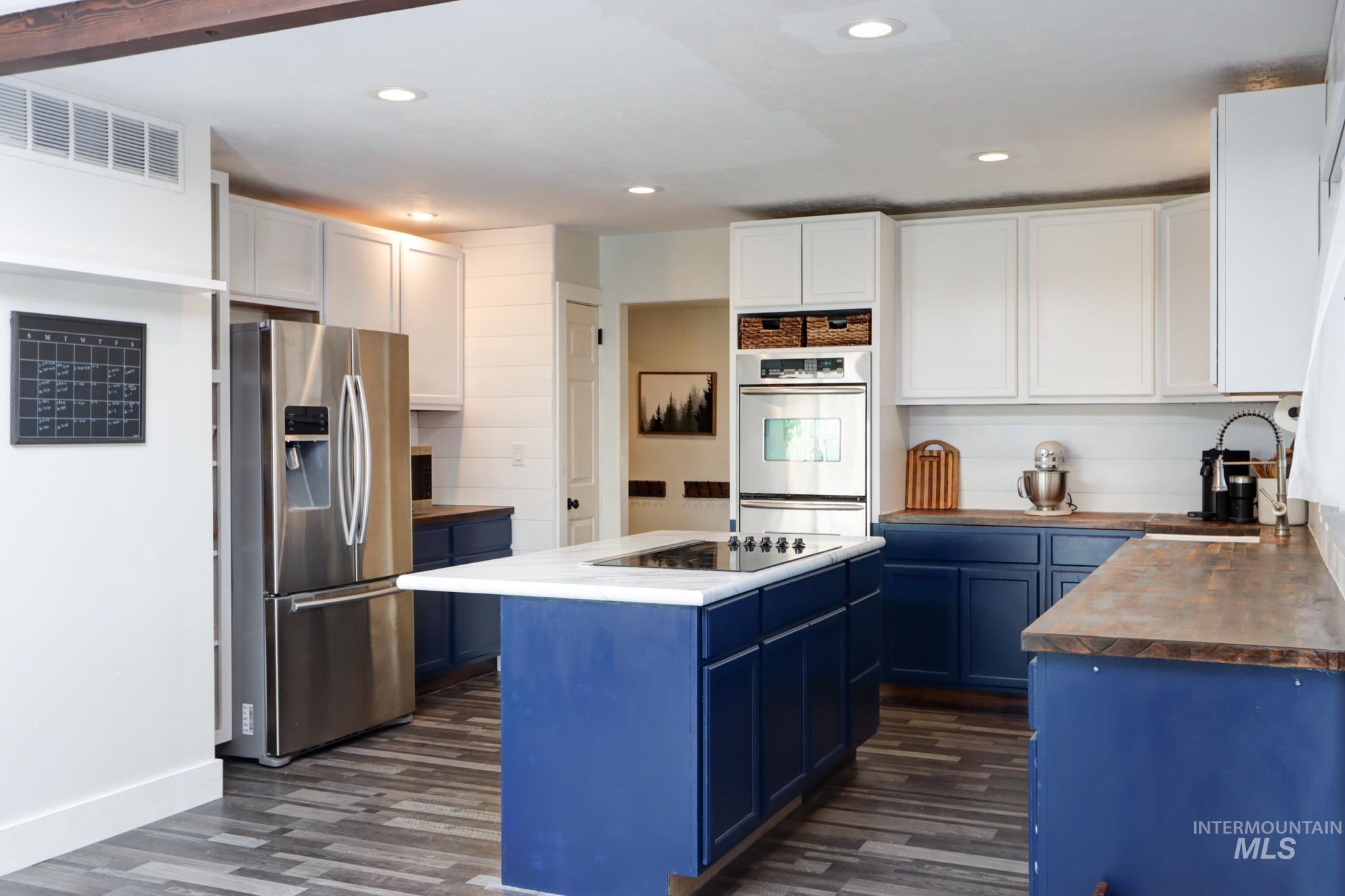 Kitchen with blue cabinets, stainless steel appliances, butcher block countertops, white cabinets, and dark wood-style flooring