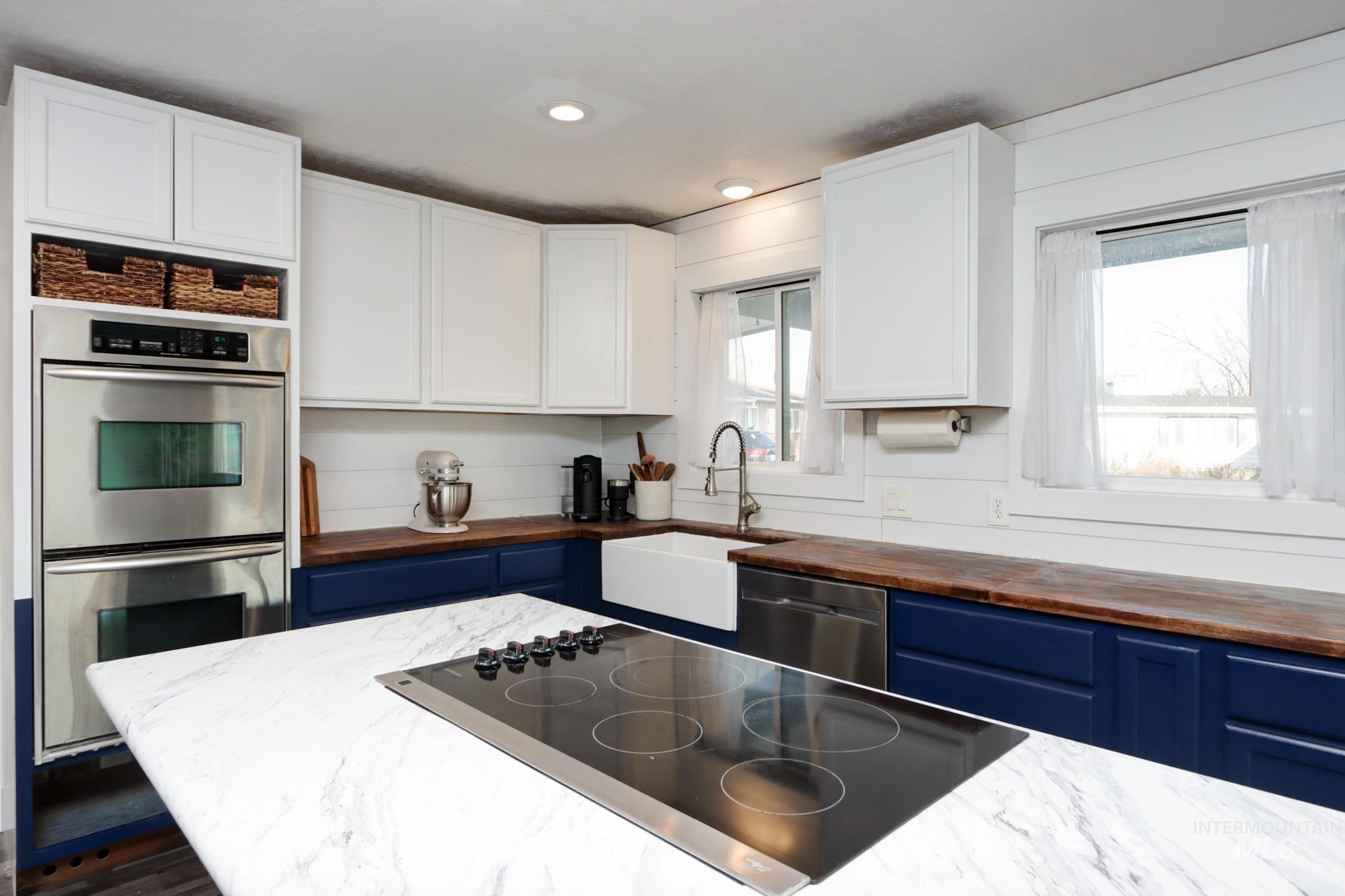 Kitchen with stainless steel appliances, butcher block counters, blue cabinets, white cabinets, and recessed lighting