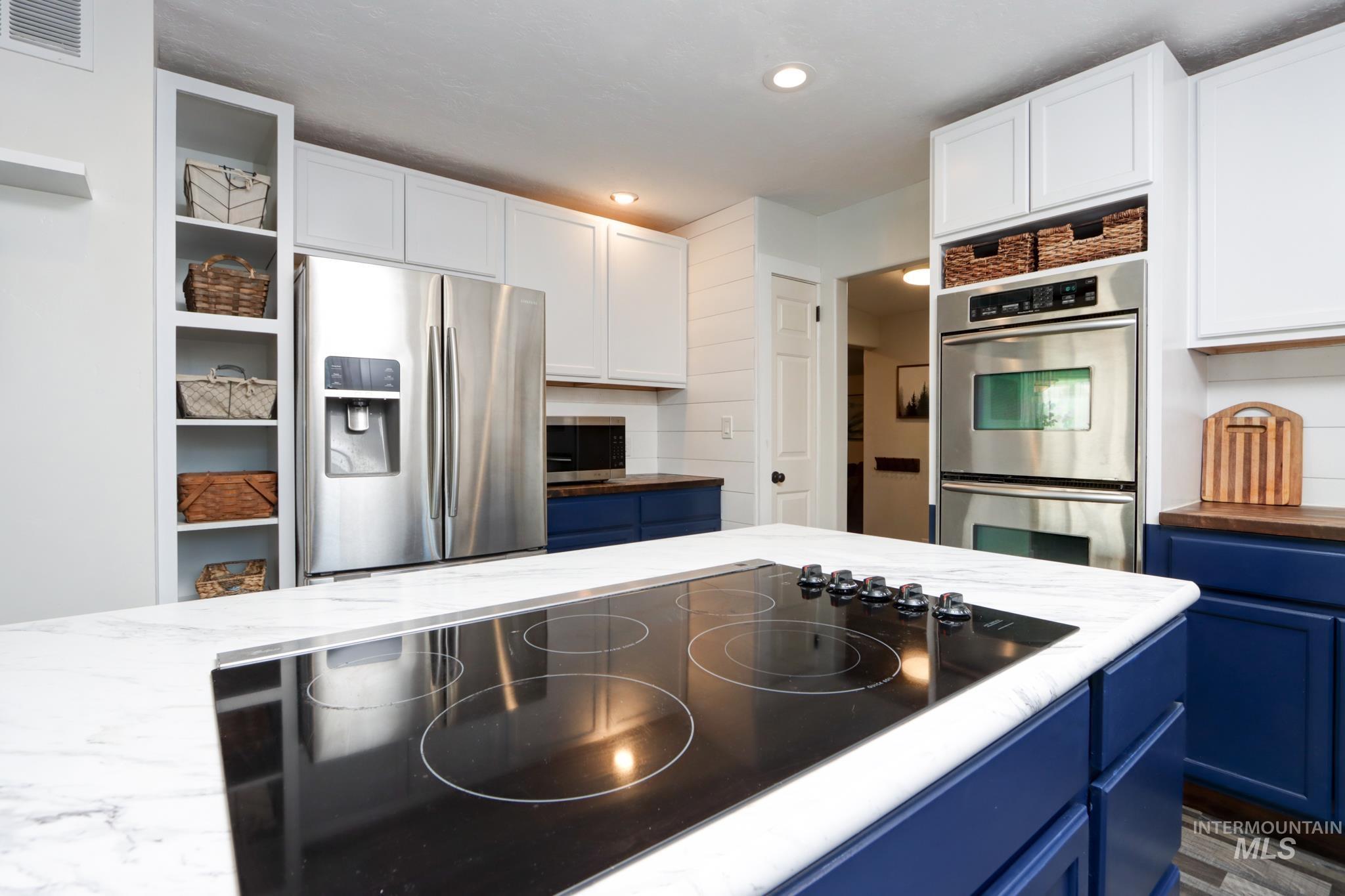 Kitchen with blue cabinets, stainless steel appliances, wooden counters, white cabinetry, and recessed lighting