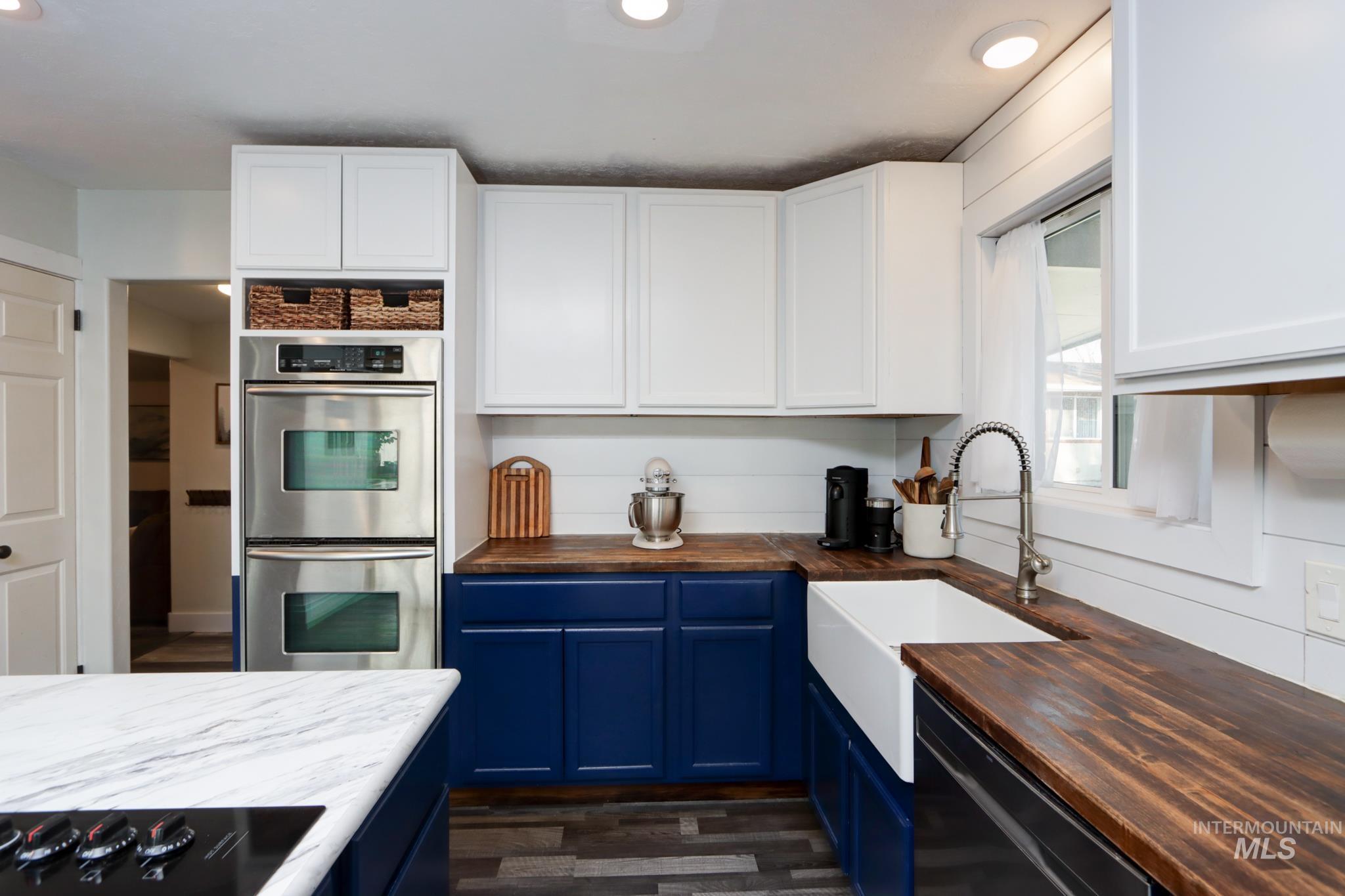 Kitchen with wooden counters, black appliances, blue cabinetry, dark wood-type flooring, and white cabinetry