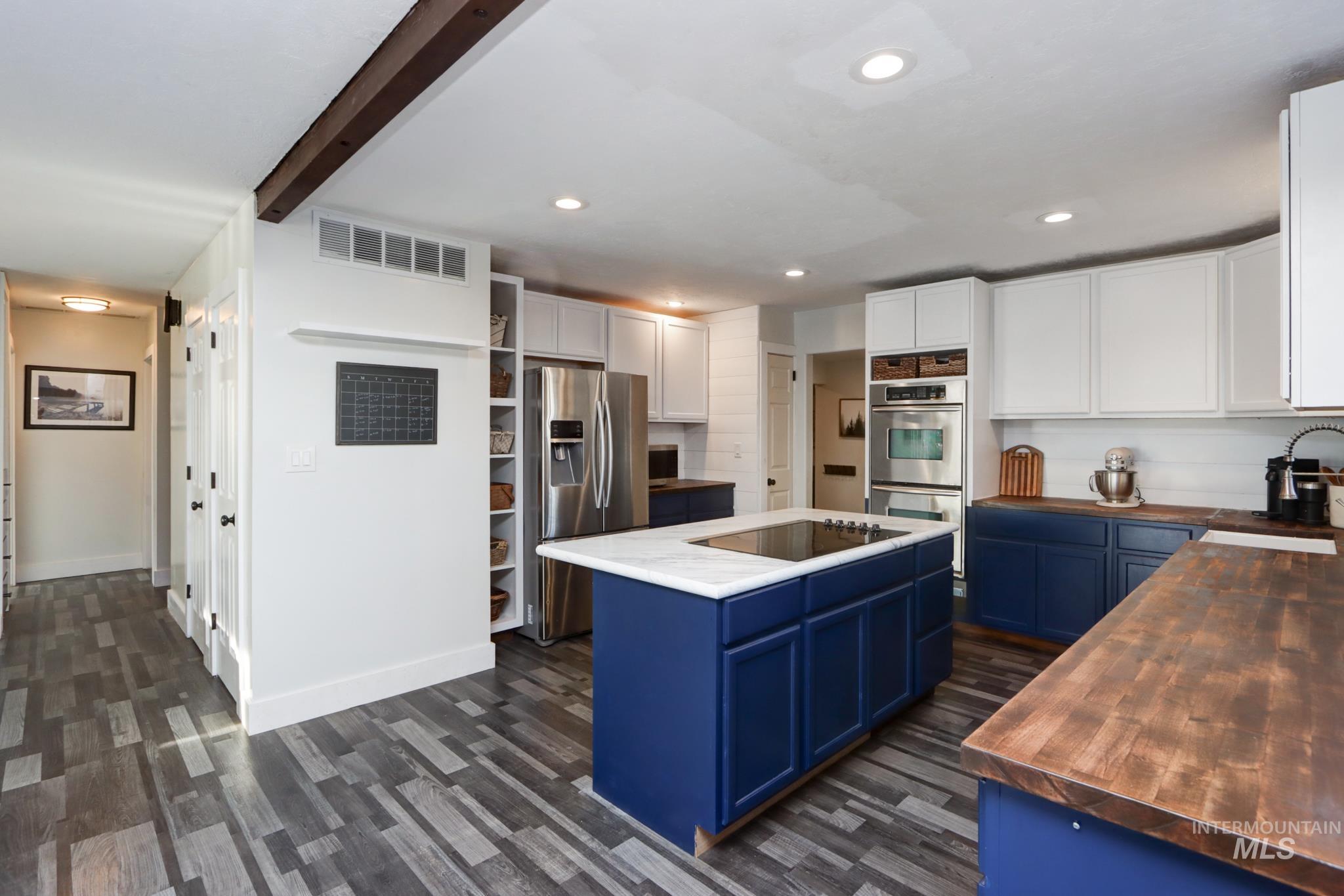 Kitchen with blue cabinets, white cabinetry, butcher block counters, stainless steel appliances, and dark wood finished floors