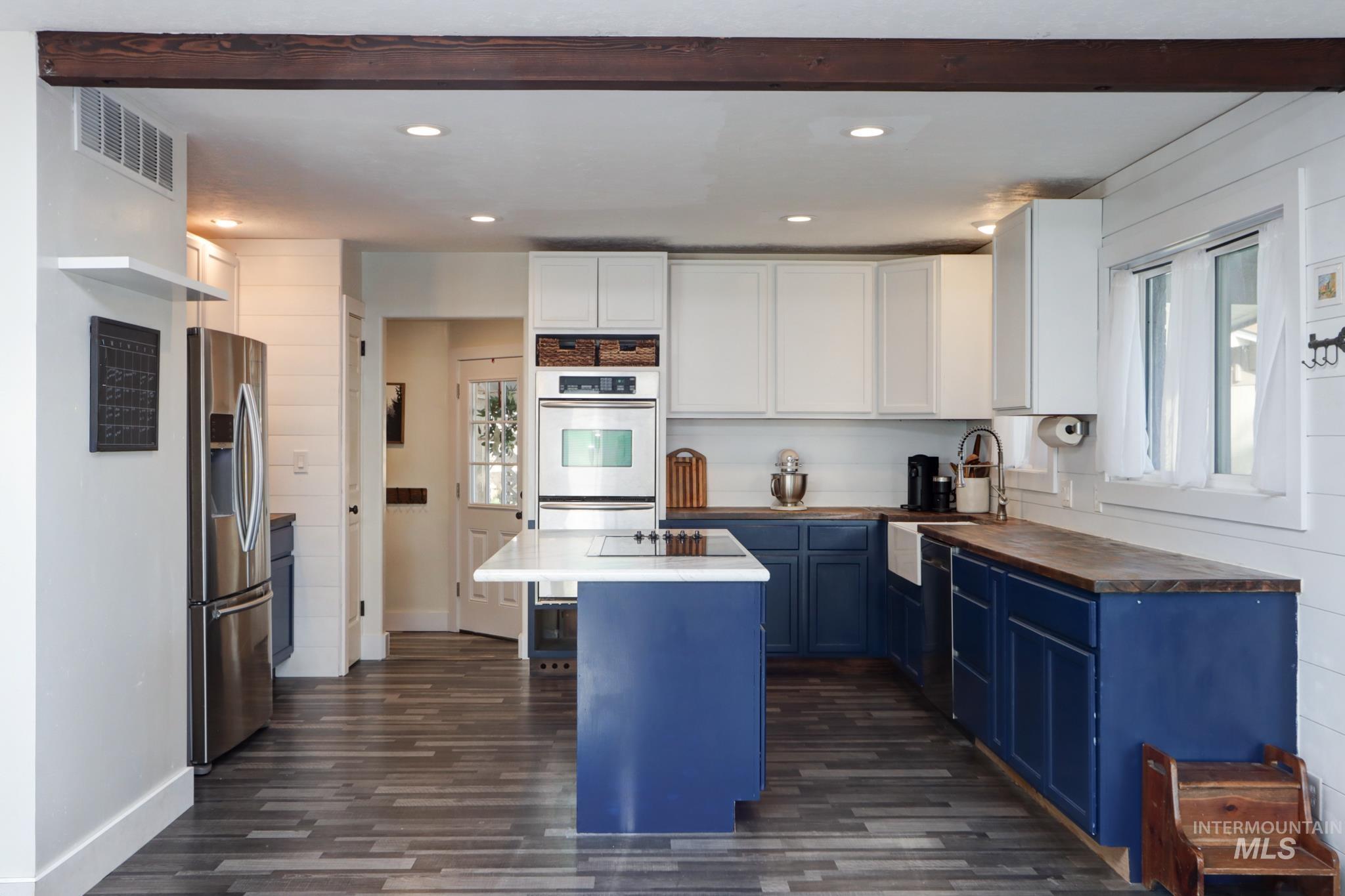 Kitchen with blue cabinets, butcher block countertops, white cabinets, stainless steel appliances, and dark wood-style floors
