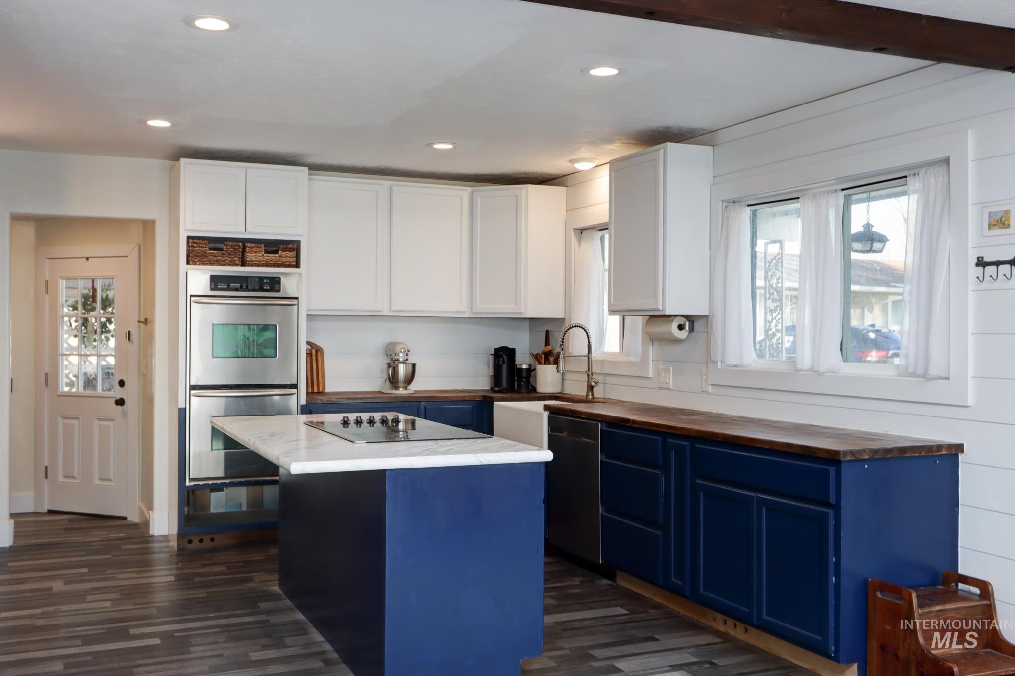 Kitchen with blue cabinets, black appliances, a center island, white cabinetry, and butcher block countertops