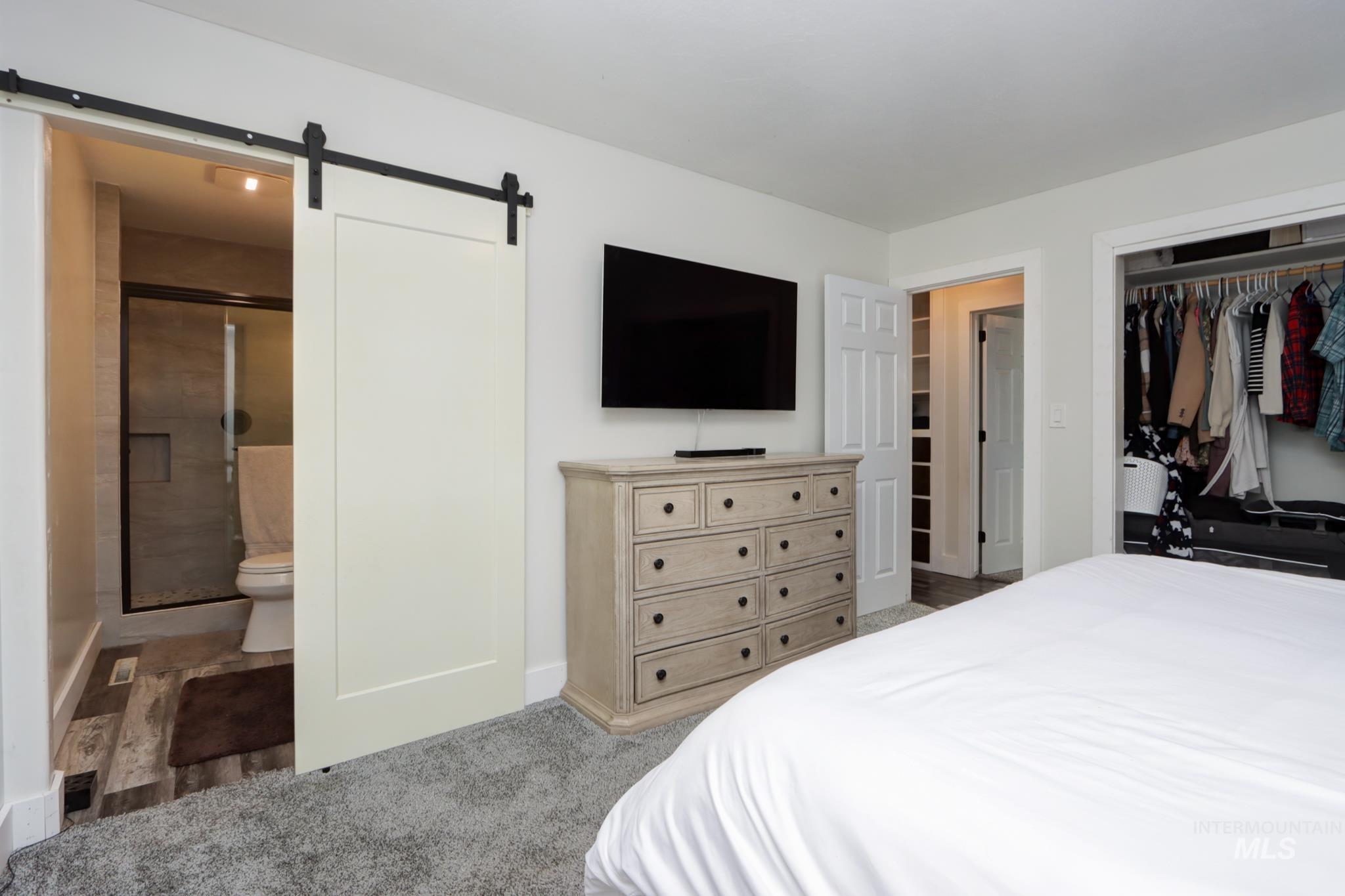 Bedroom with a barn door, a closet, connected bathroom, and light colored carpet