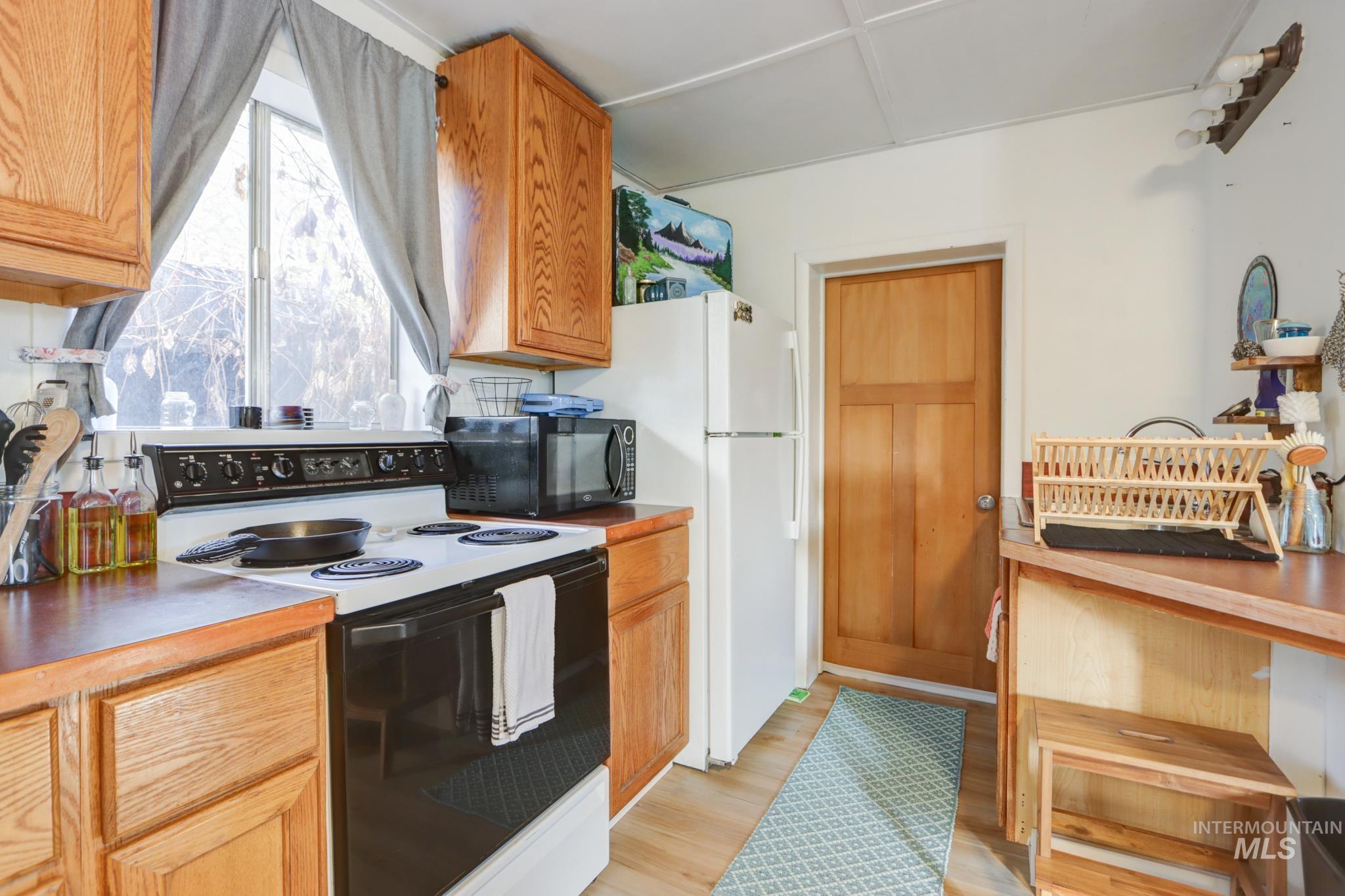 Kitchen with range with electric cooktop, black microwave, light wood-style floors, and brown cabinetry