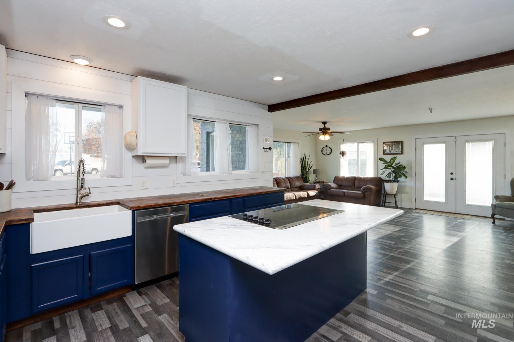 Kitchen with blue cabinetry, open floor plan, wooden counters, stainless steel dishwasher, and dark wood-style flooring