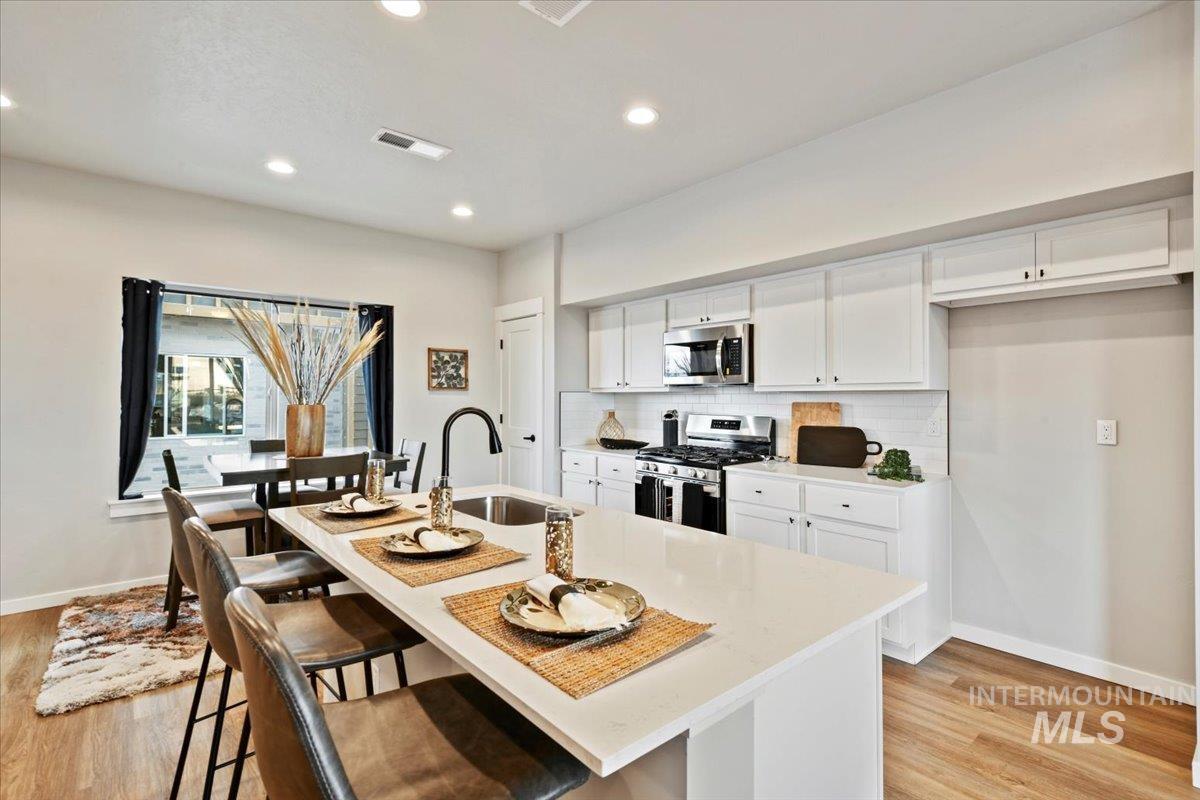 Kitchen with white cabinetry, a kitchen bar, stainless steel appliances, light wood finished floors, and recessed lighting