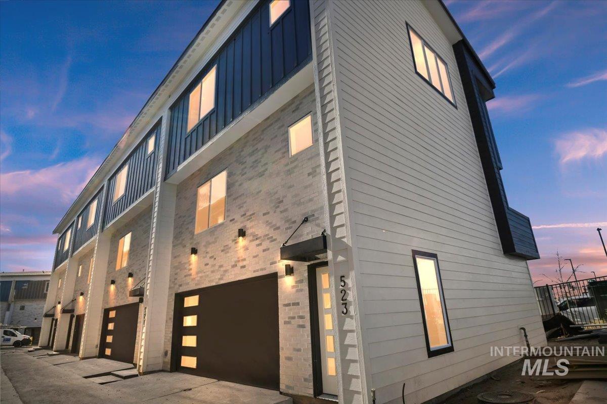 Property exterior at dusk with board and batten siding, a garage, and brick siding