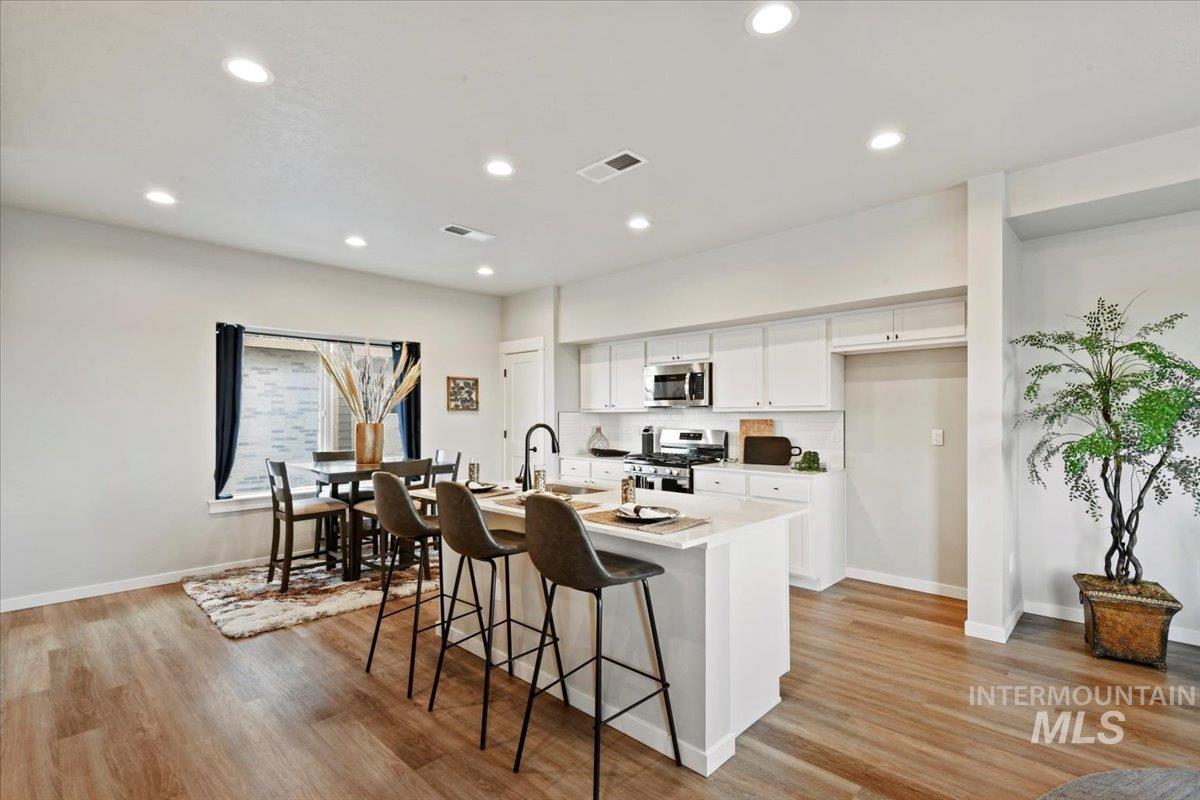 Kitchen with white cabinetry, a breakfast bar, an island with sink, stainless steel appliances, and recessed lighting