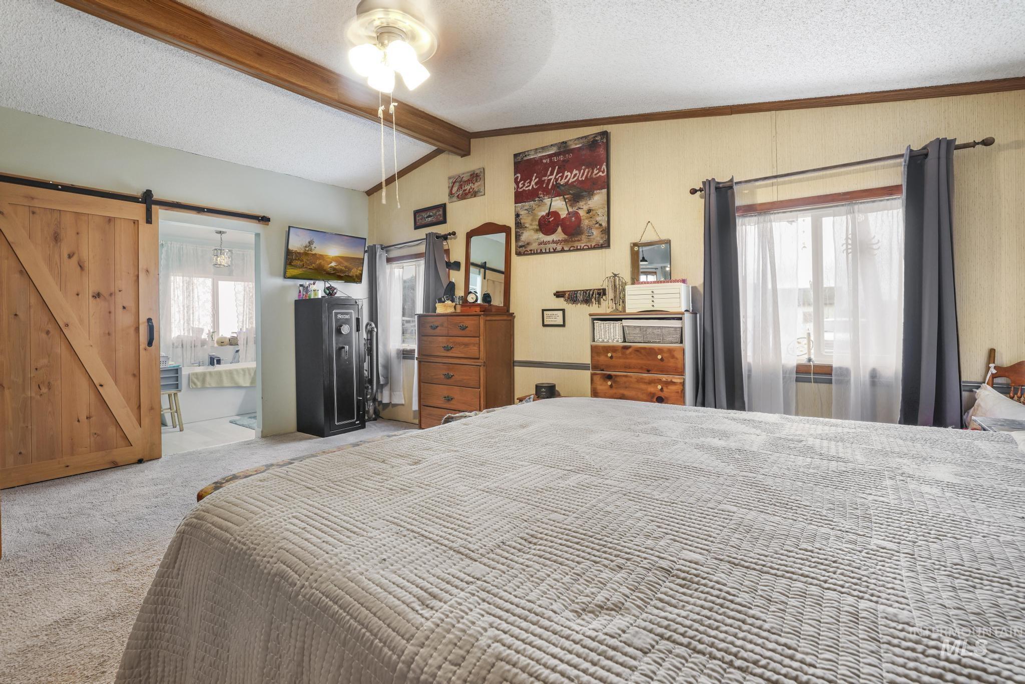 Bedroom with a textured ceiling, carpet flooring, a ceiling fan, a barn door, and connected bathroom