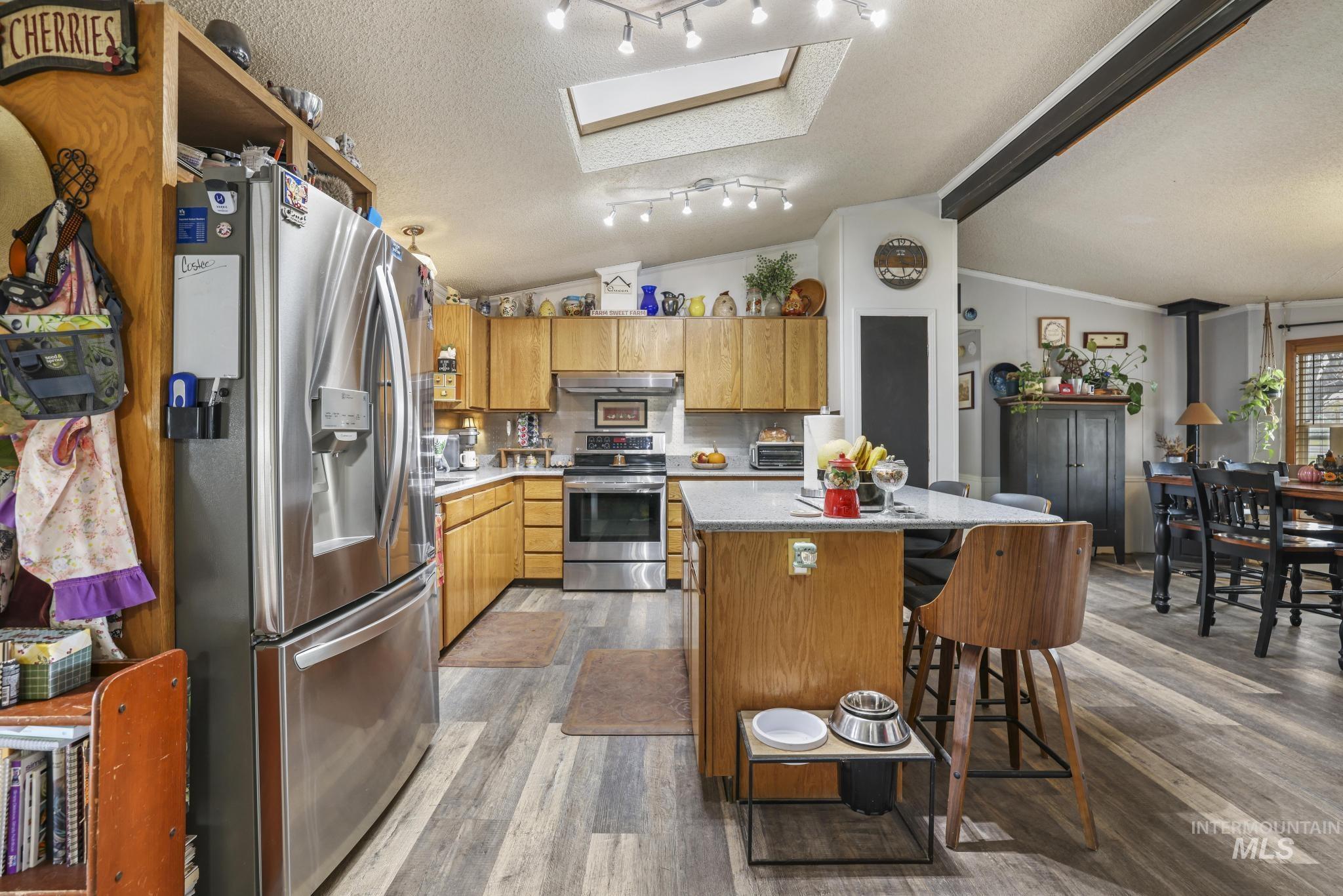 Kitchen with stainless steel appliances, a textured ceiling, a kitchen island, a breakfast bar area, and light wood-type flooring