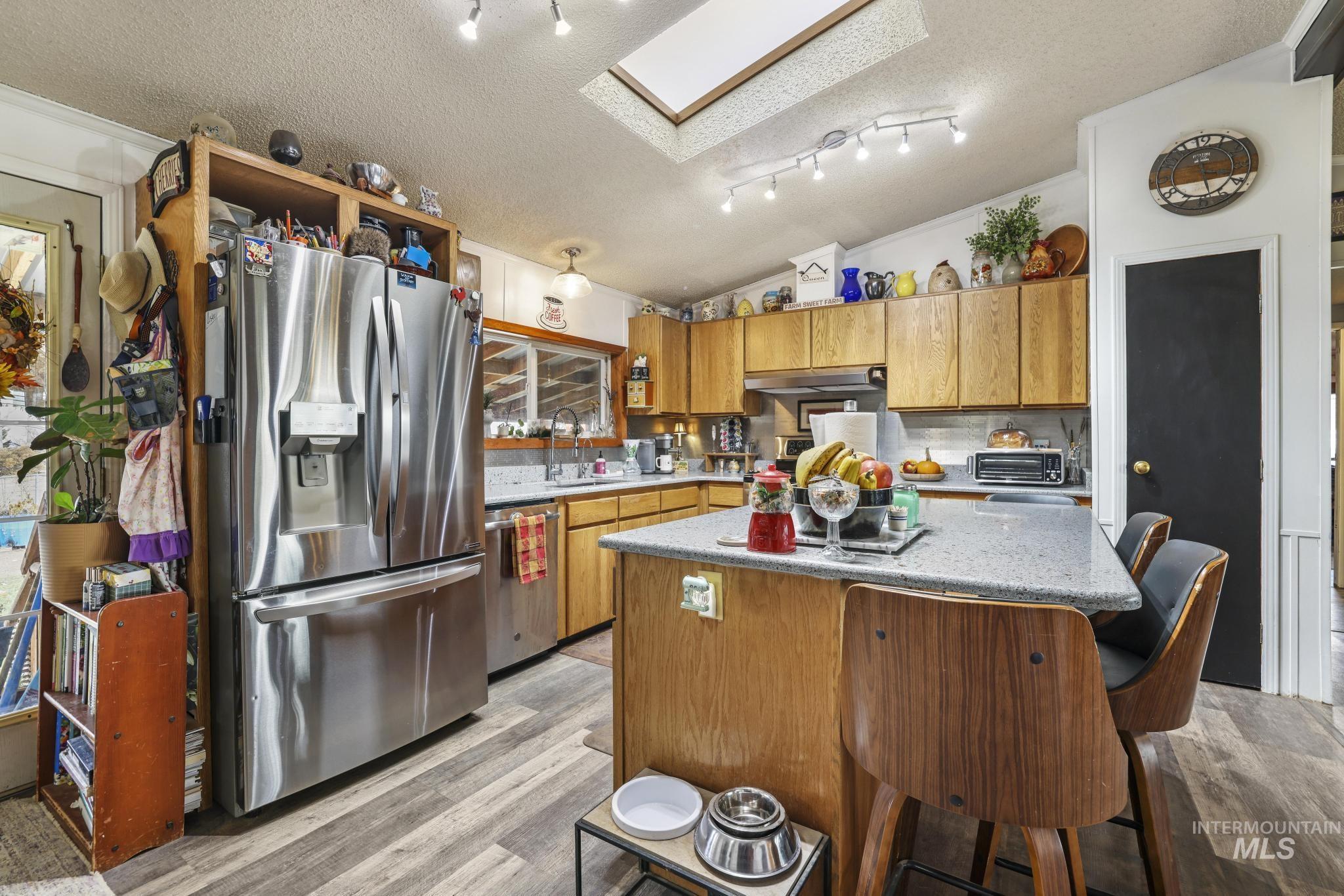 Kitchen with a breakfast bar, a textured ceiling, a skylight, appliances with stainless steel finishes, and a center island
