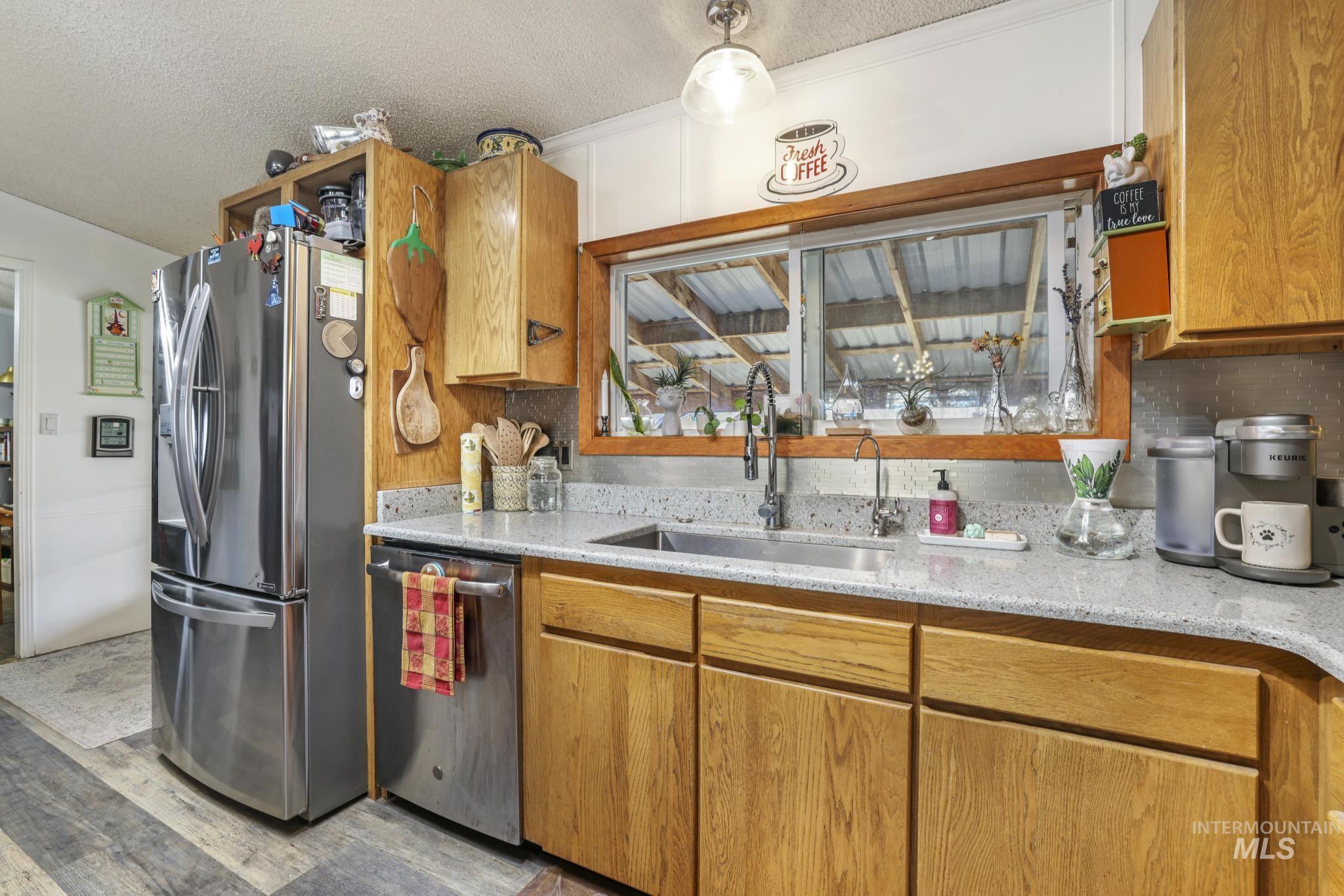 Kitchen featuring appliances with stainless steel finishes, brown cabinets, a textured ceiling, light wood-style flooring, and light stone counters