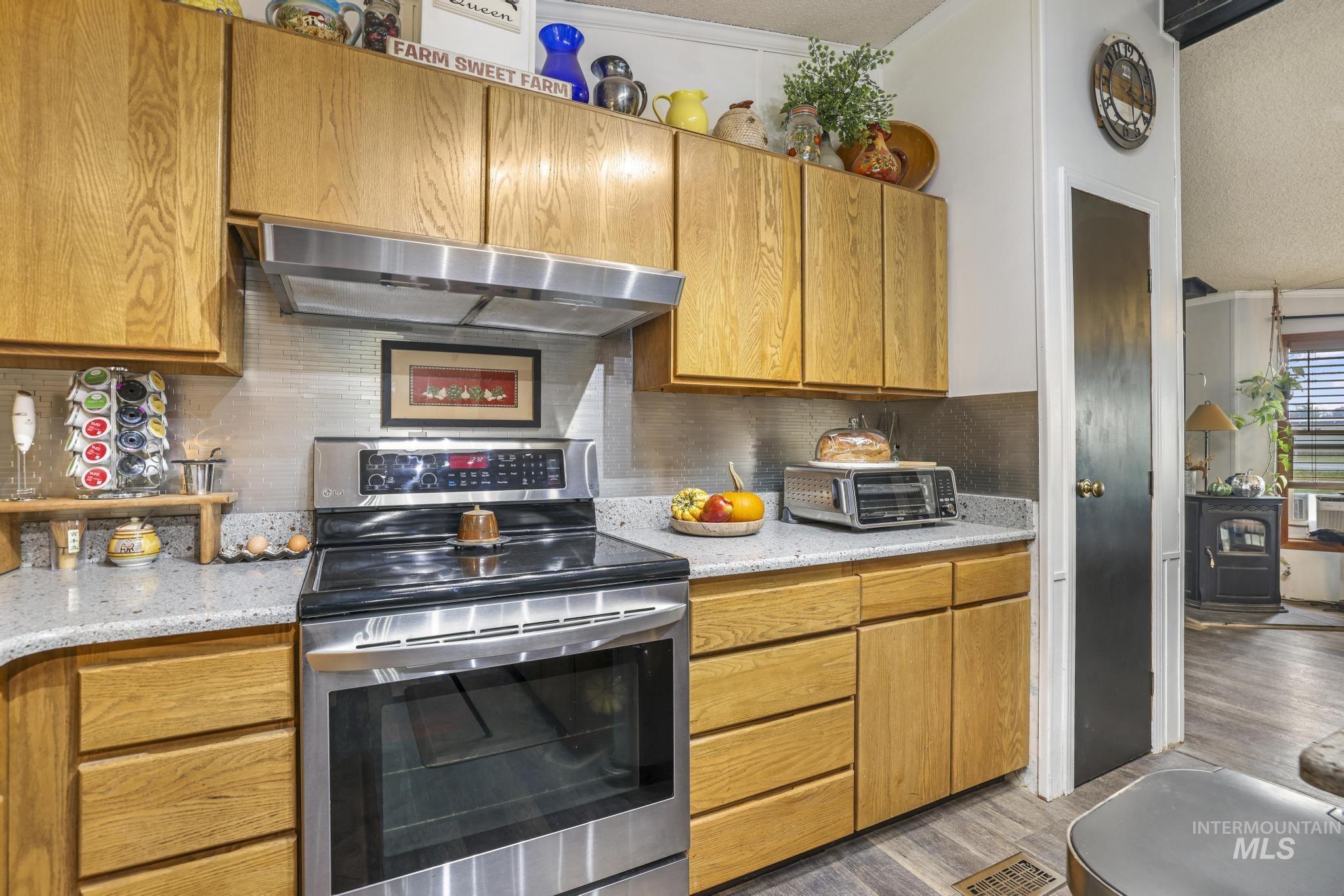 Kitchen with stainless steel range with electric cooktop, brown cabinets, decorative backsplash, wood finished floors, and light stone counters