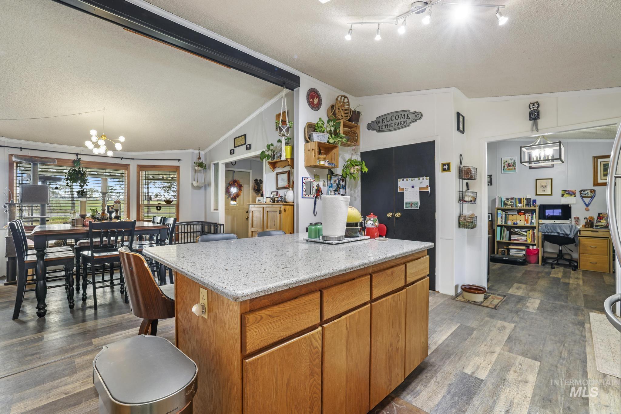 Kitchen featuring brown cabinetry, a chandelier, vaulted ceiling, decorative light fixtures, and dark wood-style flooring