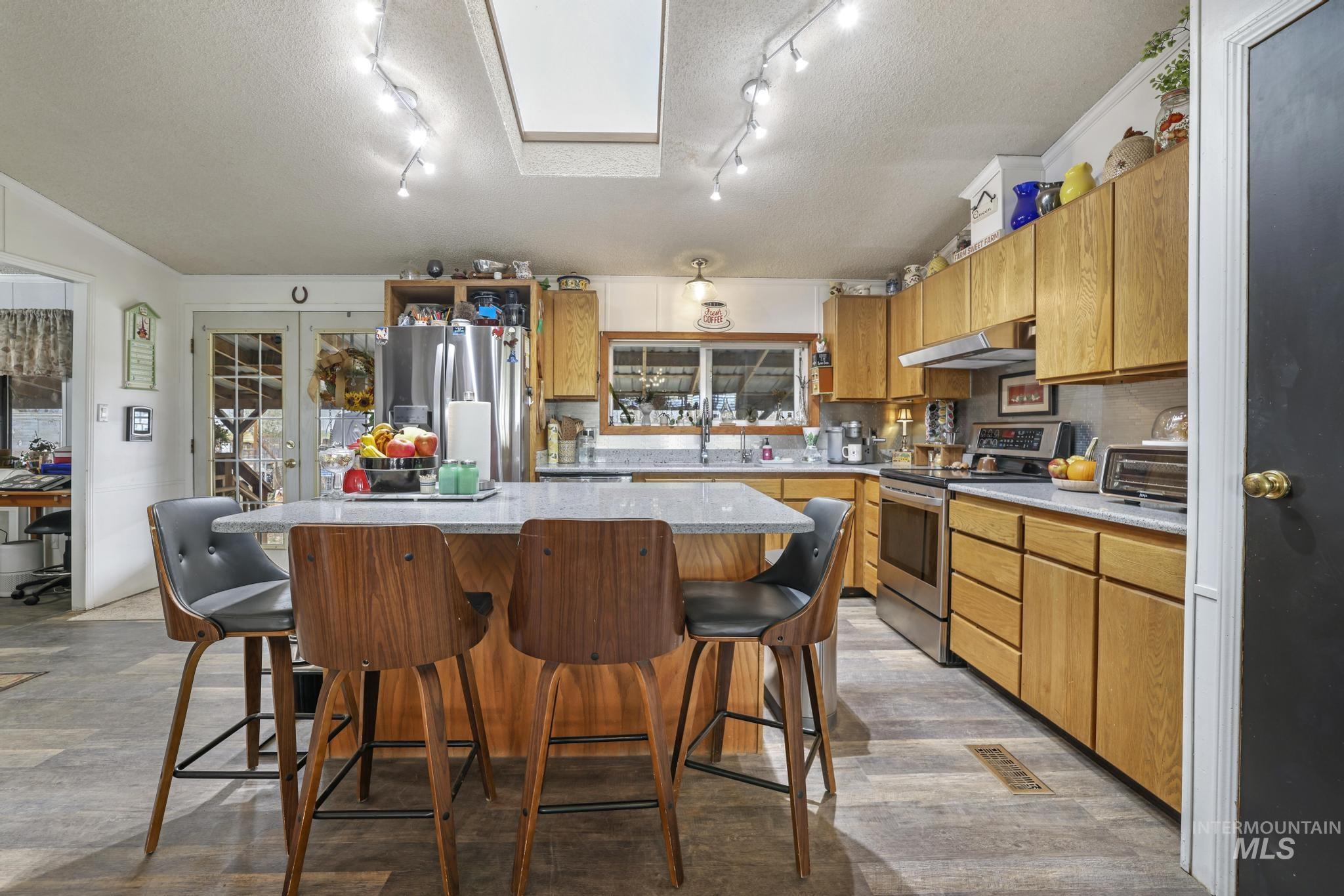 Kitchen featuring a kitchen island, stainless steel appliances, a textured ceiling, brown cabinets, and a kitchen bar