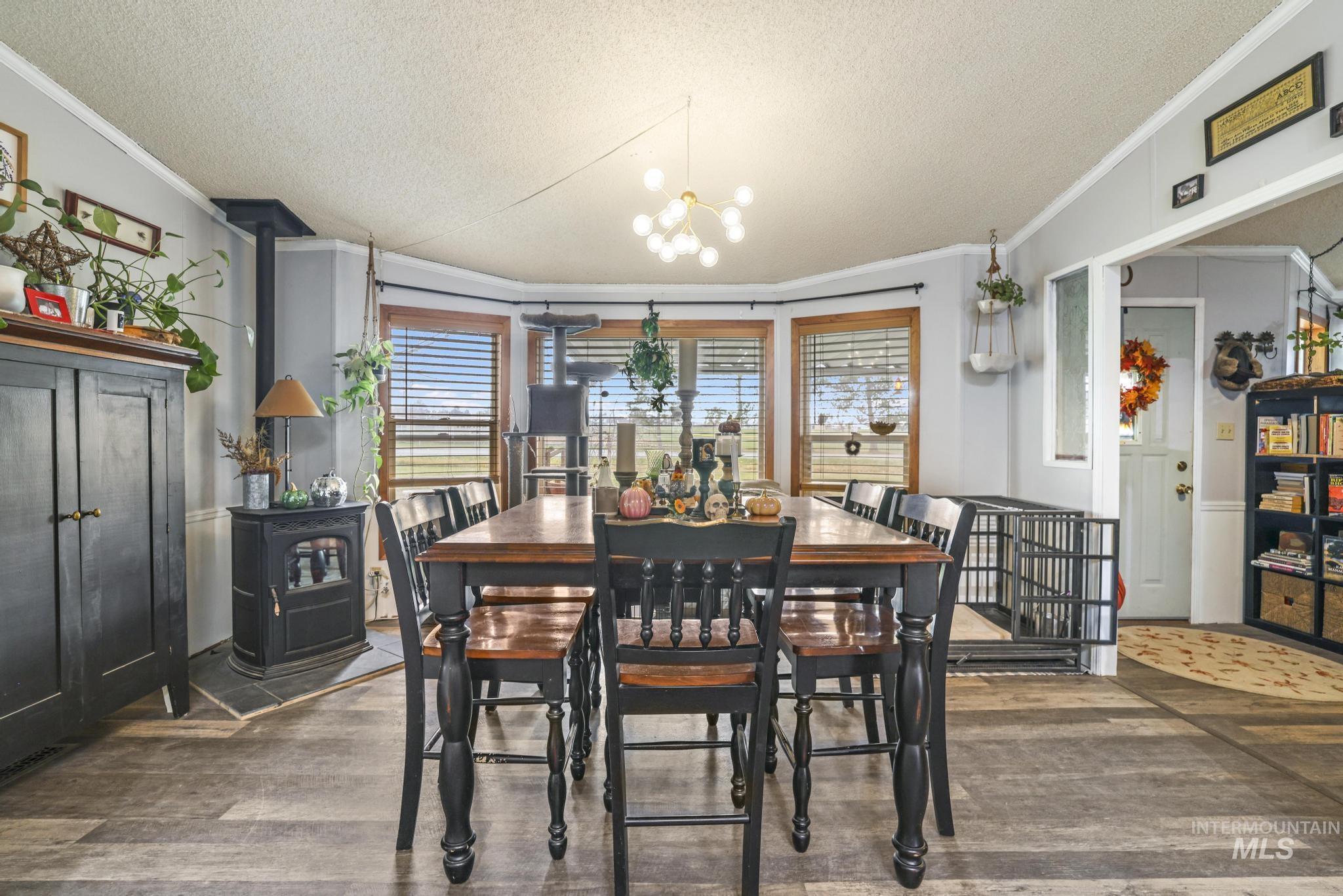 Dining room featuring a wood stove, a textured ceiling, a chandelier, wood finished floors, and crown molding