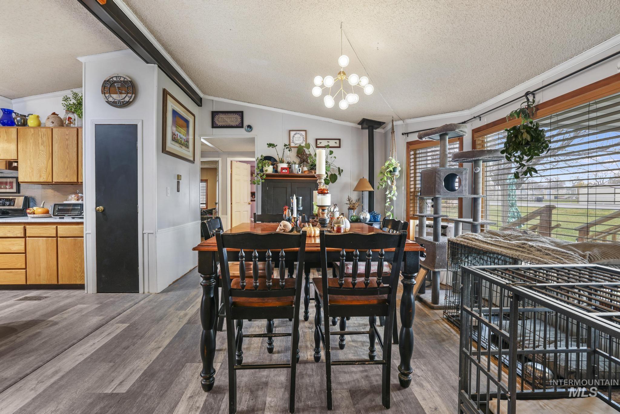 Dining area with a textured ceiling, dark wood-style floors, a chandelier, vaulted ceiling, and crown molding