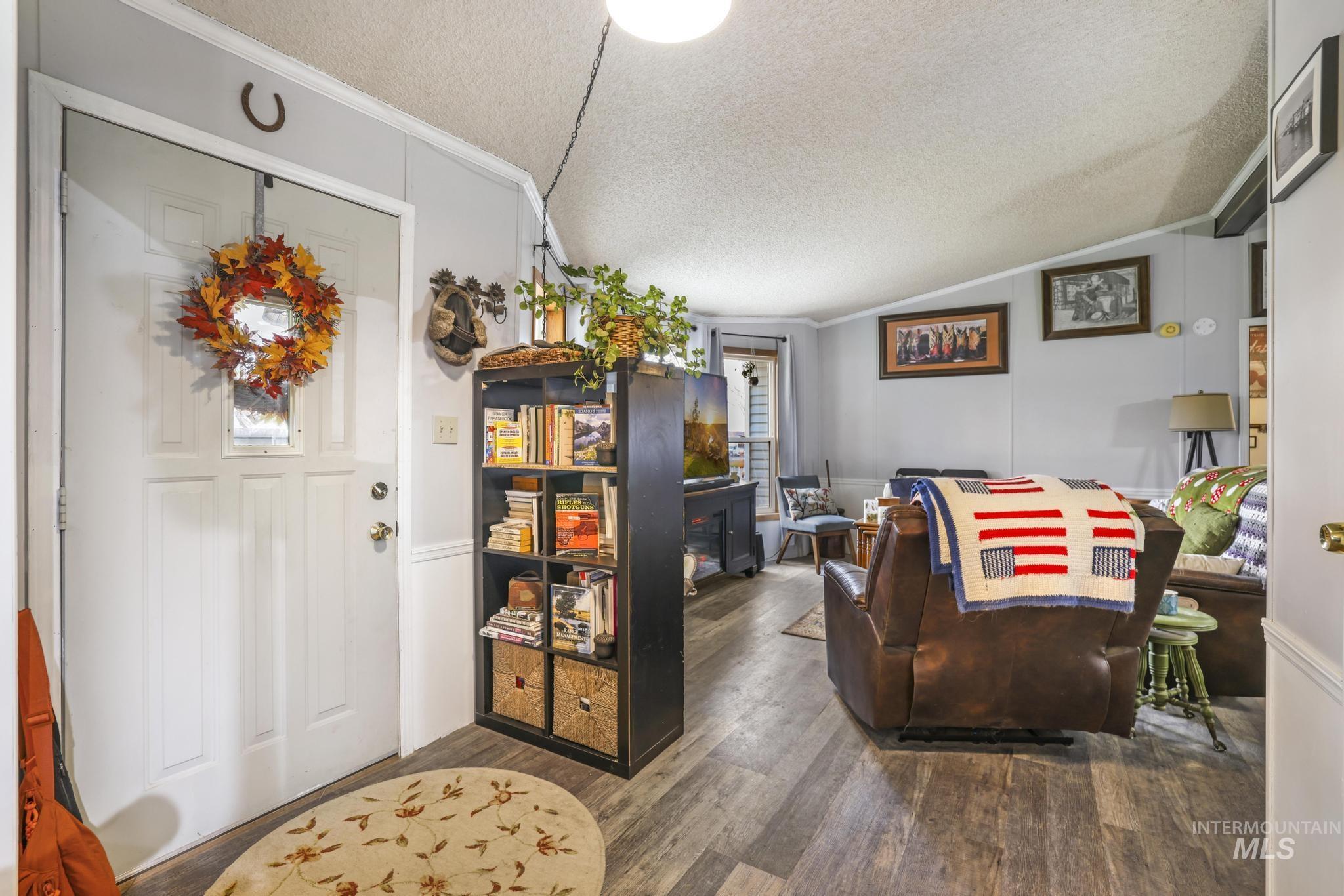 Main entry of home featuring a textured ceiling, lofted ceiling, wood finished floors, and crown molding