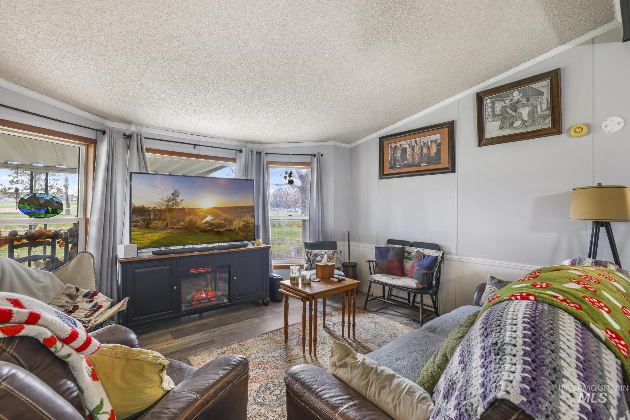 Living area with a textured ceiling, wood finished floors, ornamental molding, lofted ceiling, and a glass covered fireplace