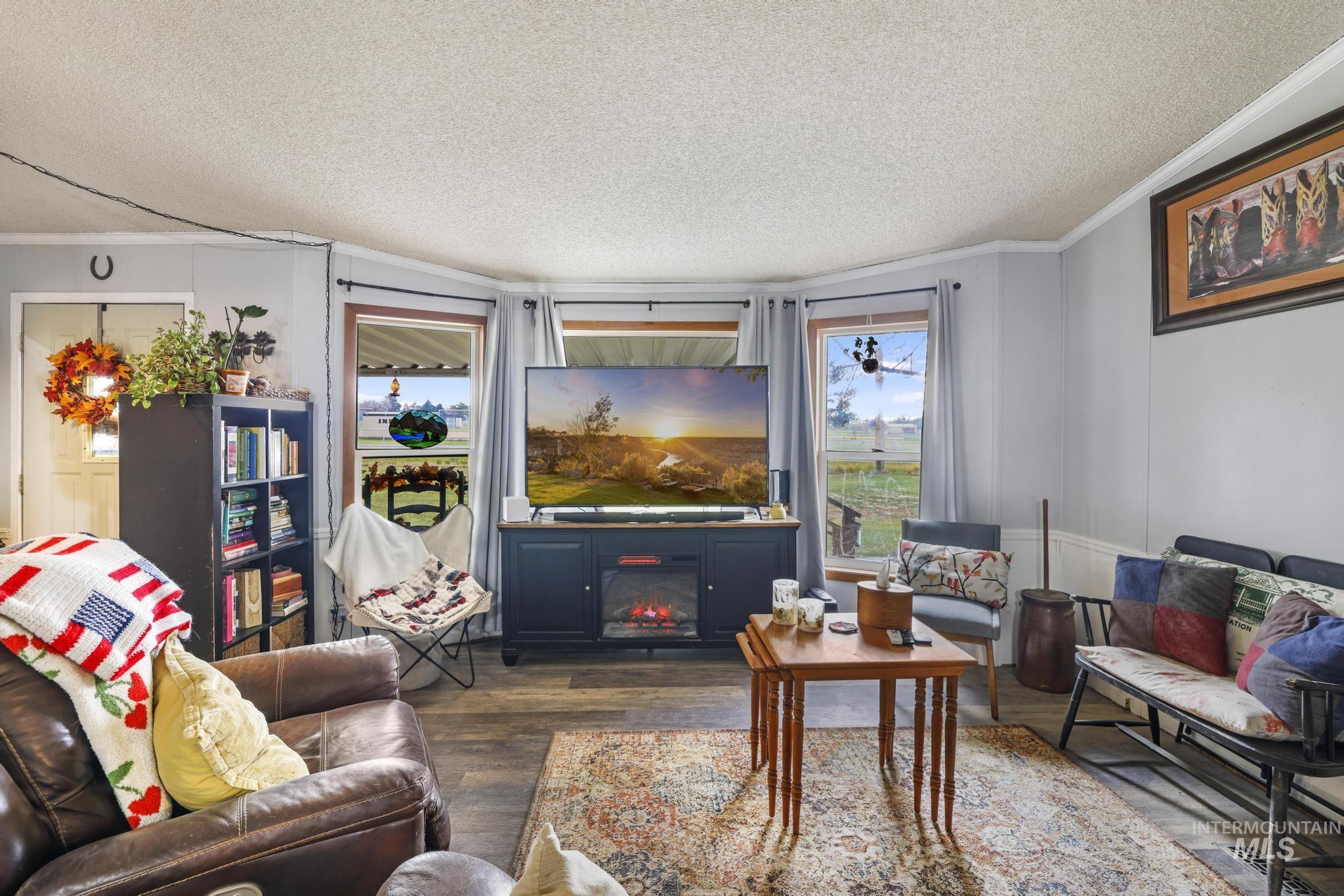 Living area with dark wood-type flooring, a textured ceiling, plenty of natural light, crown molding, and a glass covered fireplace