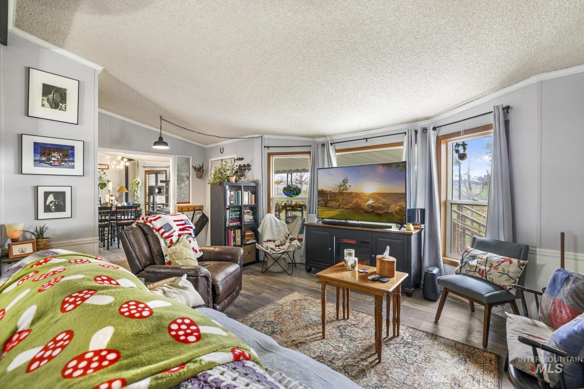 Living area featuring a textured ceiling, plenty of natural light, wood finished floors, lofted ceiling, and crown molding
