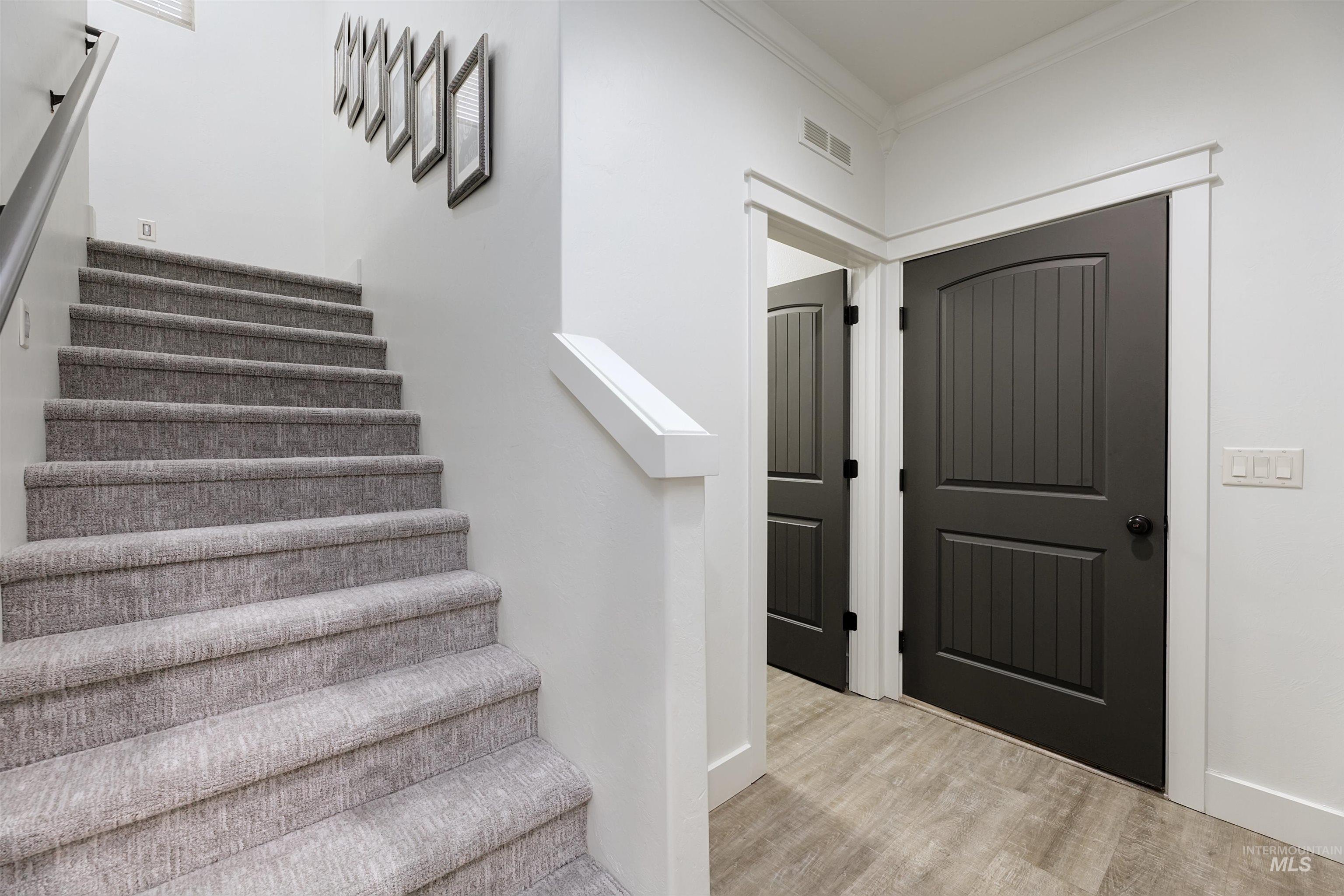 Carpeted staircase, wood finished floors, hallway leading to both the garage and laundry room.