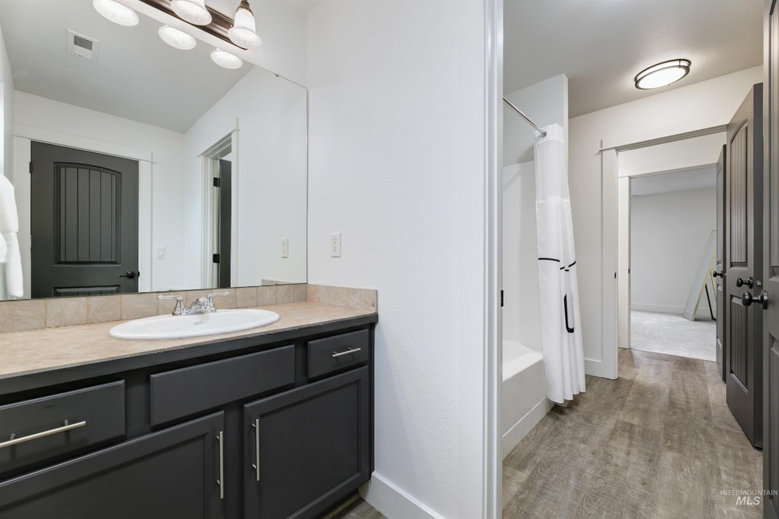 Full Jack and Jill bathroom connecting two guest bedrooms with a vanity, tub/shower combo, and light wood flooring.