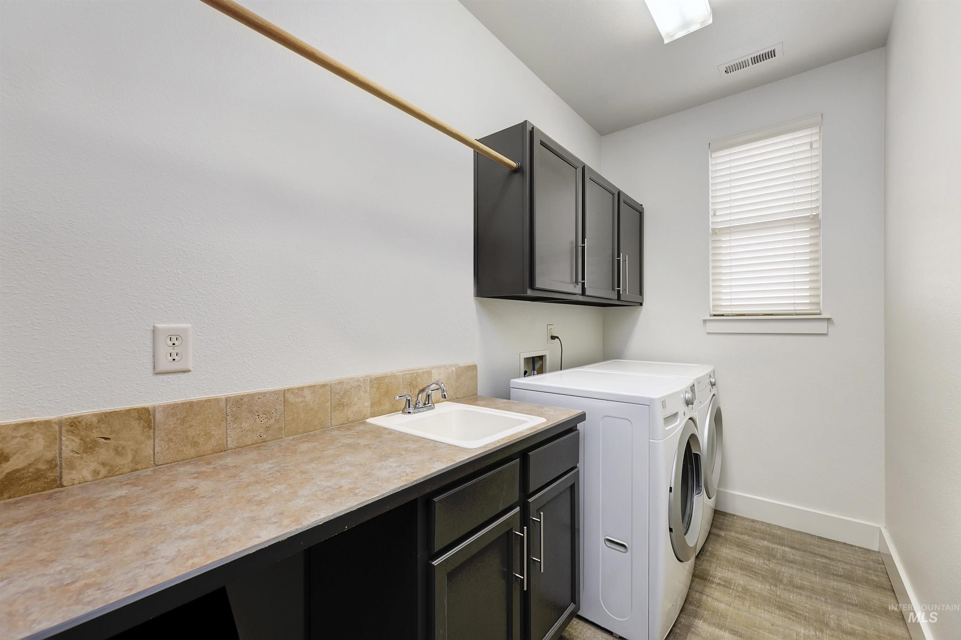 Spacious laundry room with ample counter and hanging space. Offers storage cabinets as well as washer and dryer.