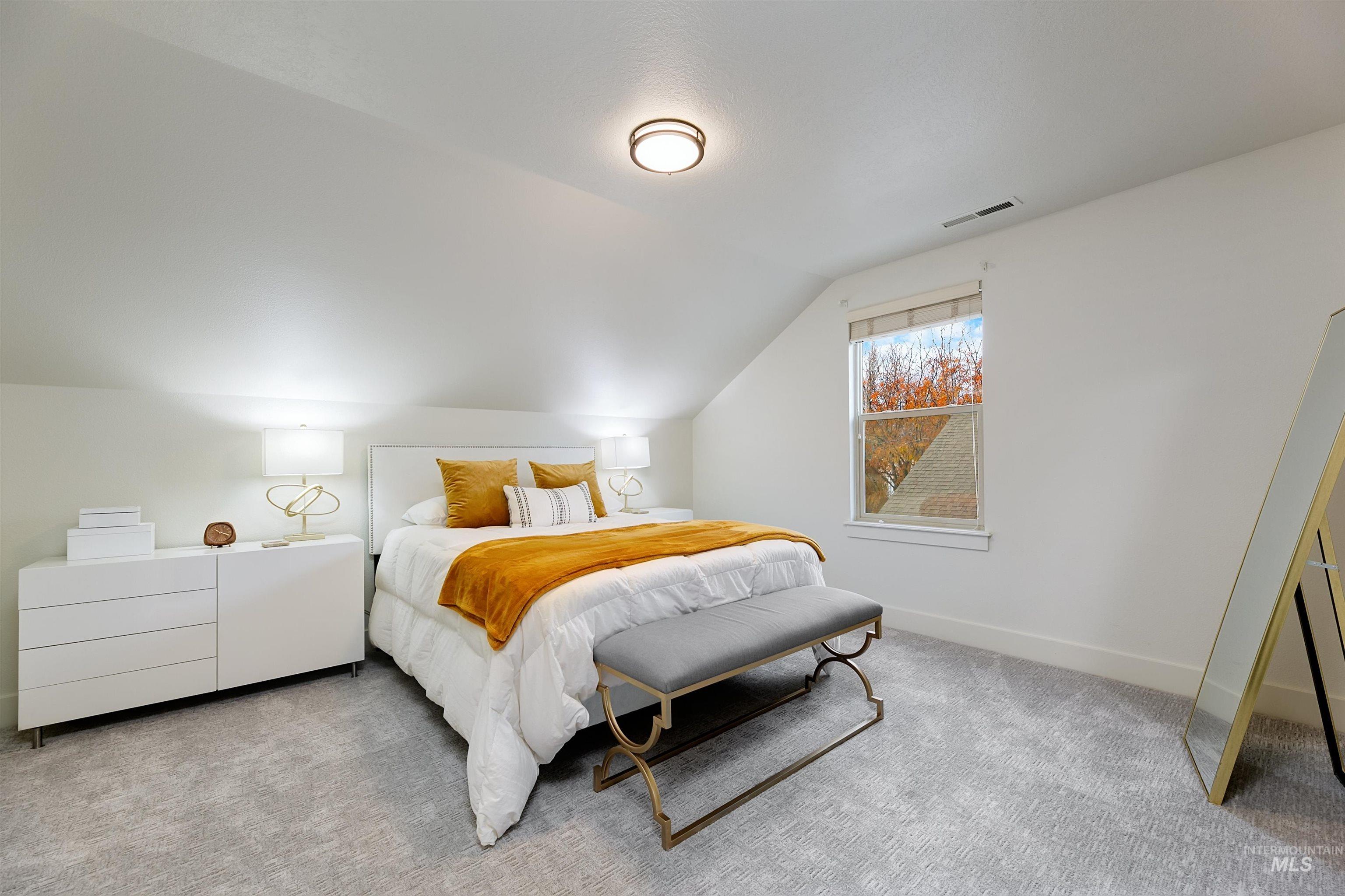 Bedroom featuring lofted ceiling and carpet flooring, warm accents, and natural light.
