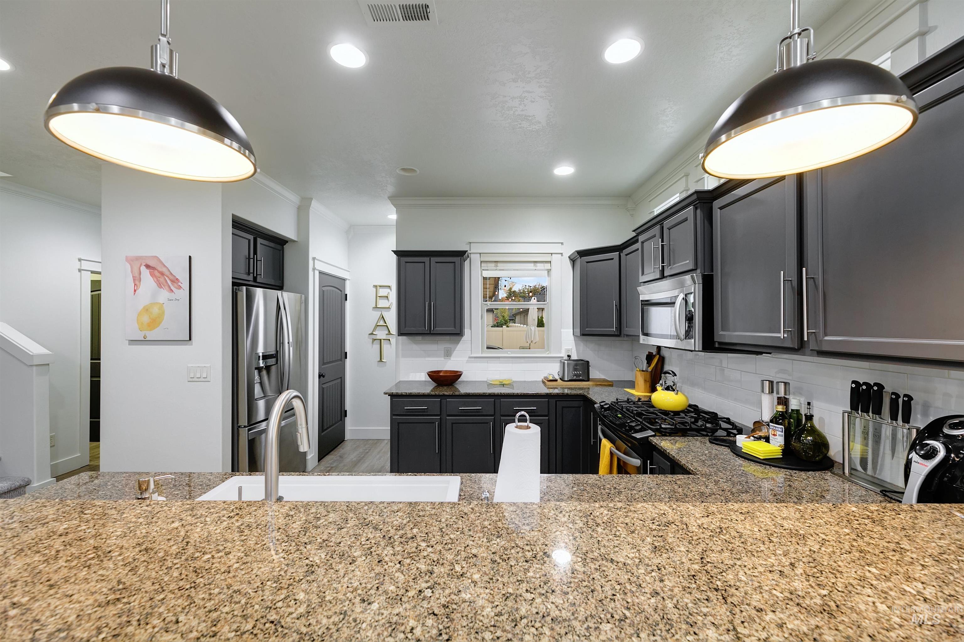 Kitchen with pendant lighting, subway tile backsplash, granite countertops with bar top seating.