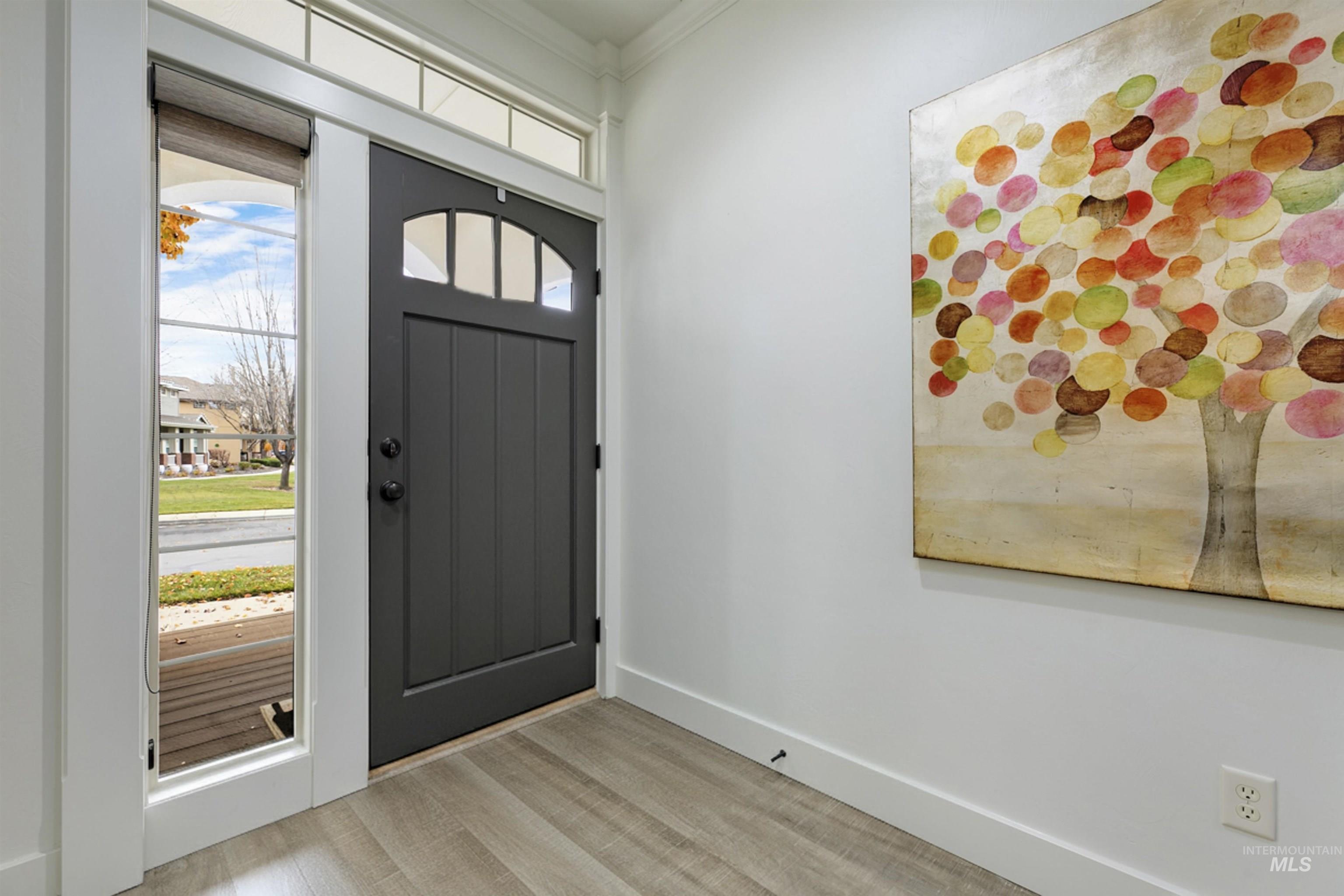 The bright entryway features a modern front door with side windows that bring in natural light. The clean design and warm flooring create a welcoming first impression as you enter the home.