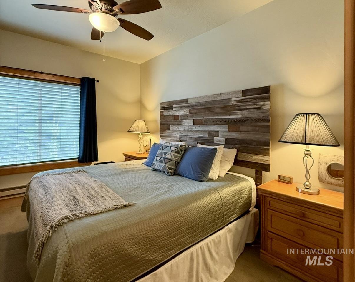 Bedroom with ceiling fan, carpet flooring, and baseboard heating
