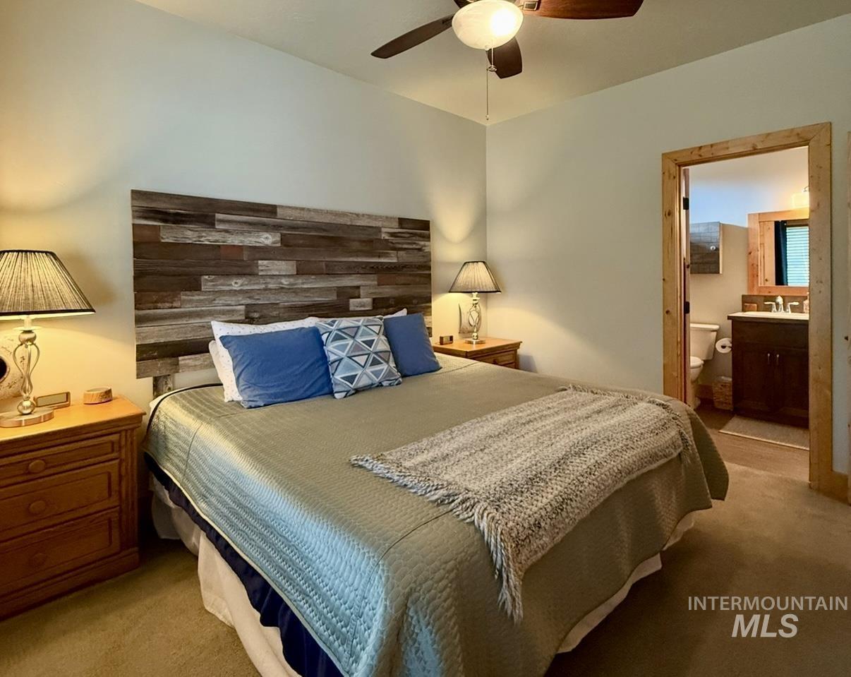 Bedroom featuring light carpet, ensuite bath, and a ceiling fan