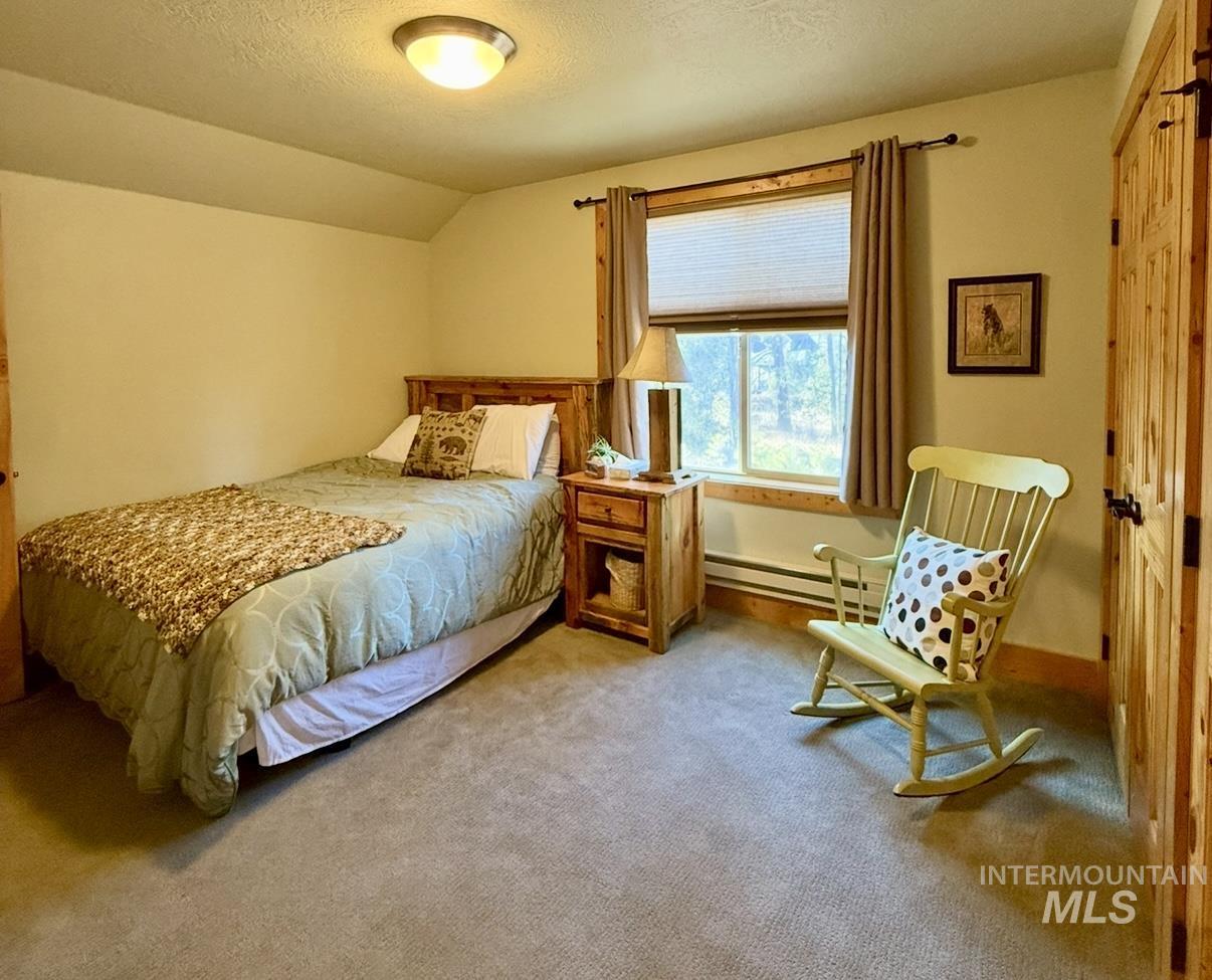 Carpeted bedroom featuring a textured ceiling, vaulted ceiling, and baseboard heating