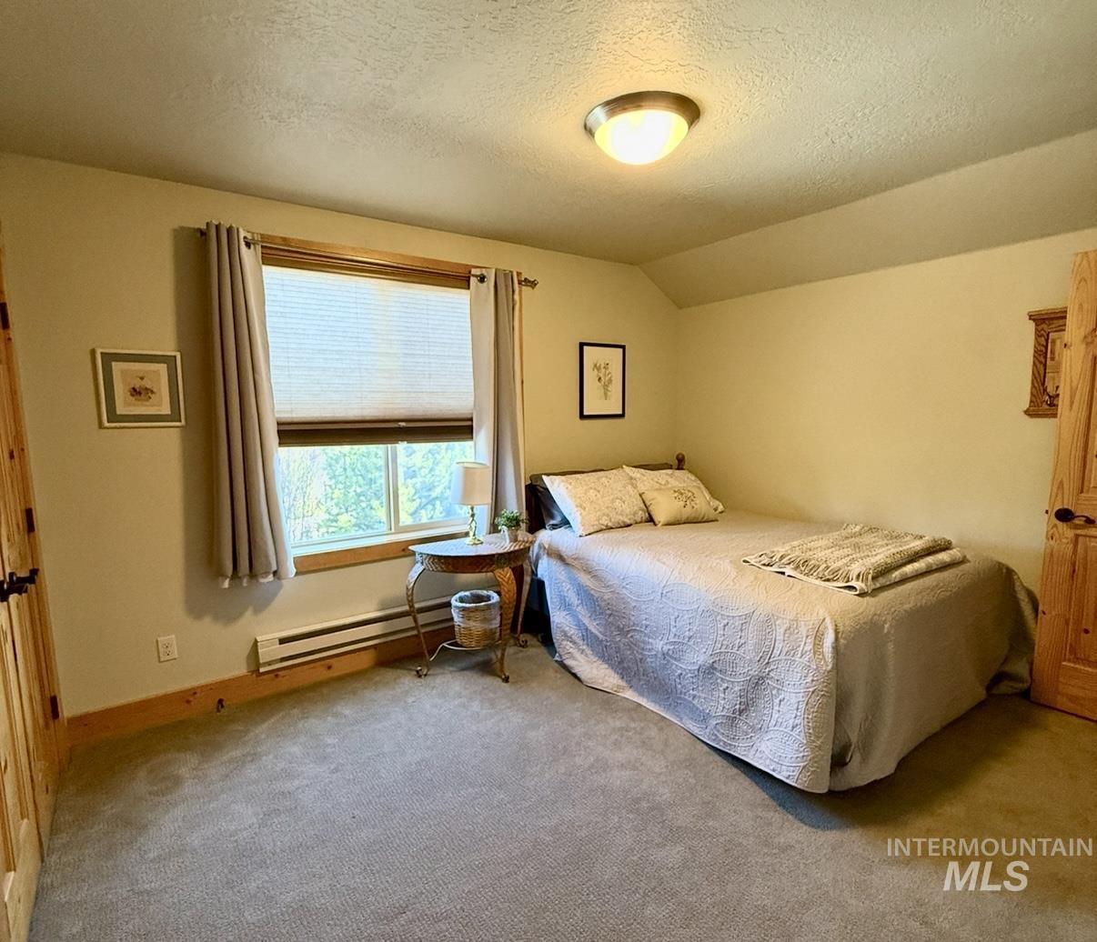 Carpeted bedroom with a textured ceiling, lofted ceiling, and a baseboard heating unit
