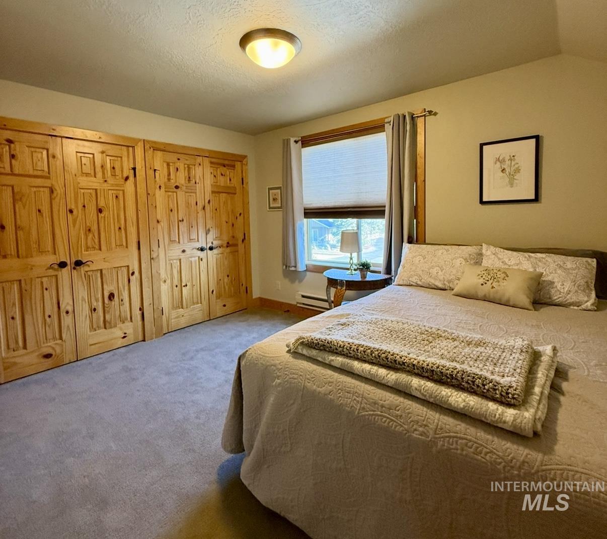 Carpeted bedroom featuring multiple closets, a textured ceiling, a baseboard radiator, and lofted ceiling