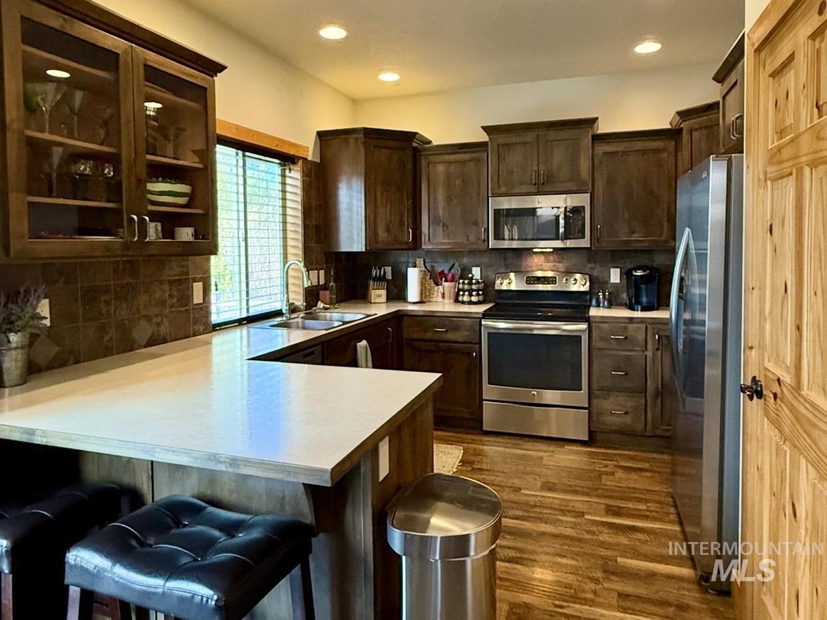Kitchen with dark brown cabinets, appliances with stainless steel finishes, light countertops, decorative backsplash, and recessed lighting