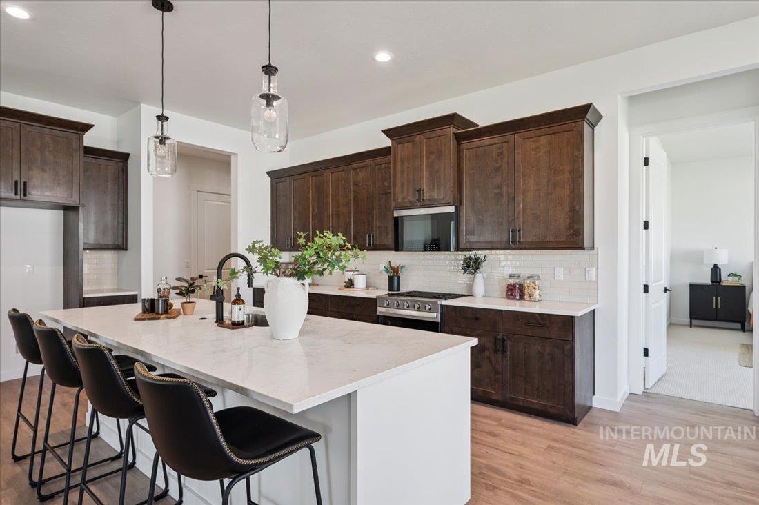 Kitchen featuring dark brown cabinets, a breakfast bar, pendant lighting, a center island with sink, and appliances with stainless steel finishes