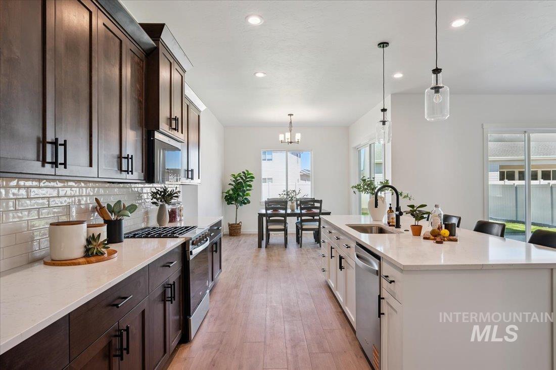 Kitchen with light stone countertops, dark brown cabinetry, appliances with stainless steel finishes, decorative light fixtures, and recessed lighting