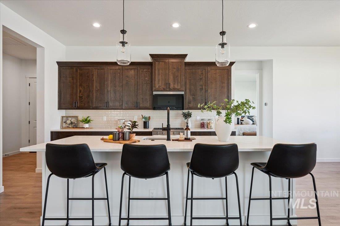 Kitchen with light wood finished floors, tasteful backsplash, hanging light fixtures, recessed lighting, and dark brown cabinets