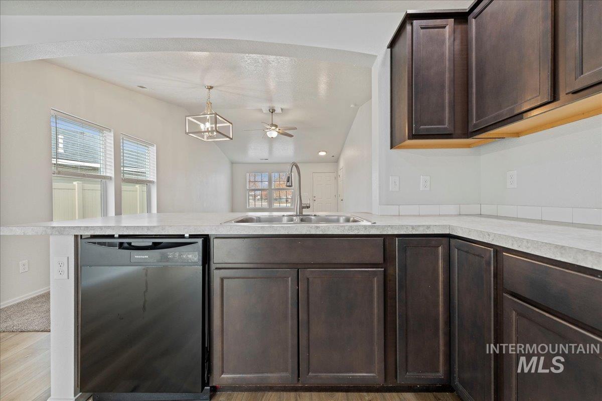 Kitchen with dark brown cabinetry, dishwasher, light countertops, lofted ceiling, and ceiling fan