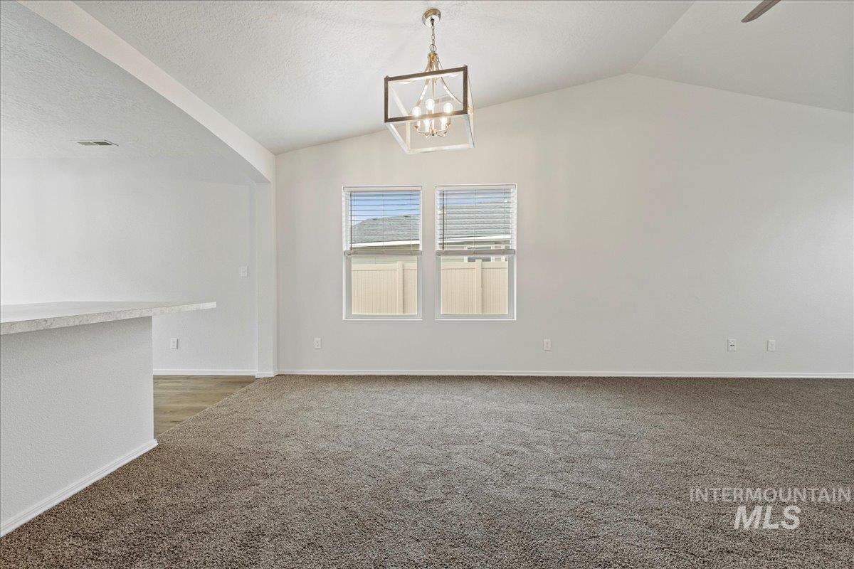 Unfurnished dining area featuring carpet flooring, vaulted ceiling, a textured ceiling, a chandelier, and a ceiling fan