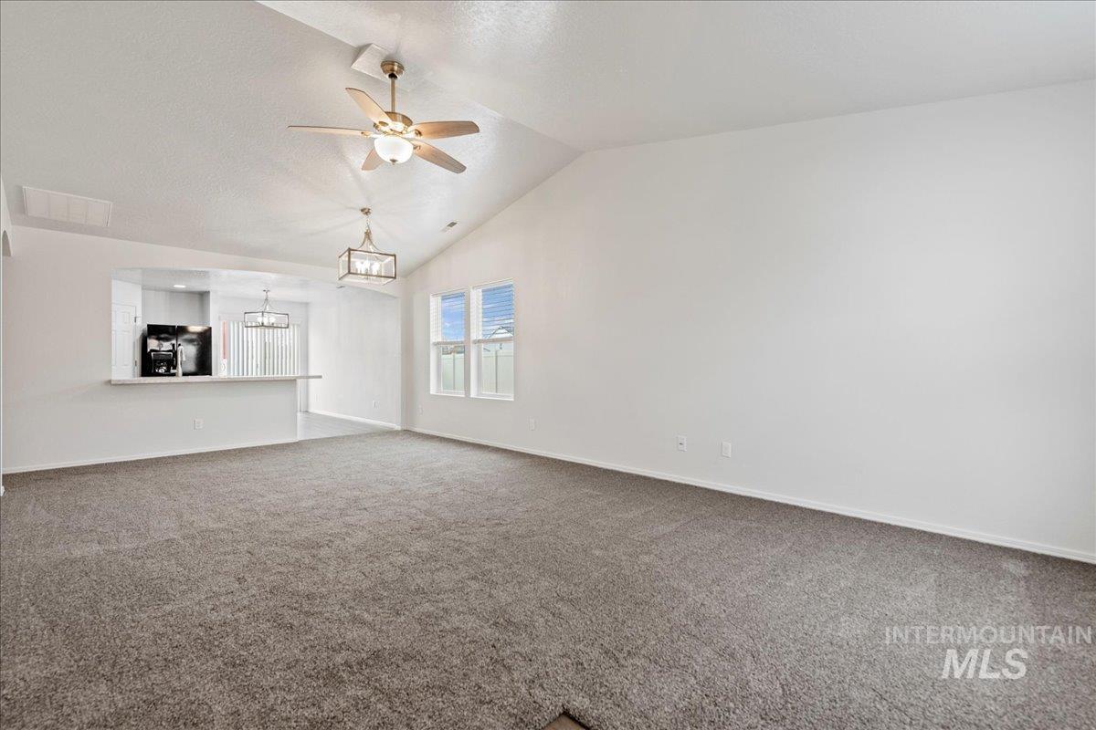 Unfurnished living room featuring ceiling fan, lofted ceiling, carpet floors, and a chandelier
