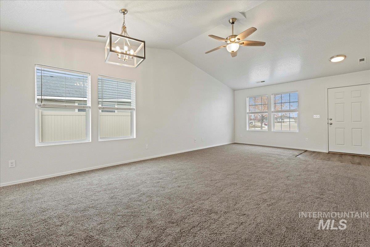 Carpeted empty room featuring ceiling fan, vaulted ceiling, and a textured ceiling