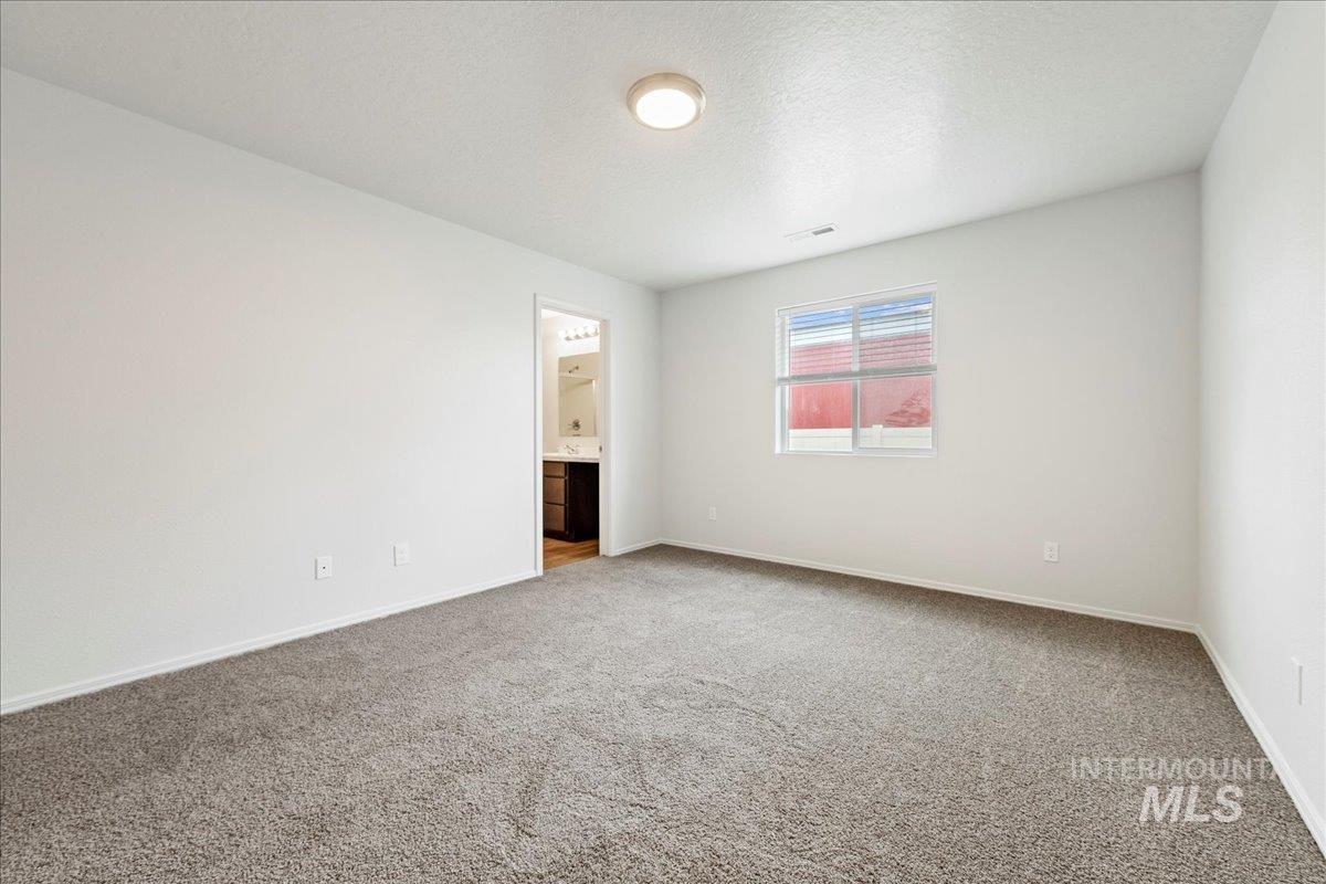 Carpeted spare room featuring a textured ceiling and baseboards